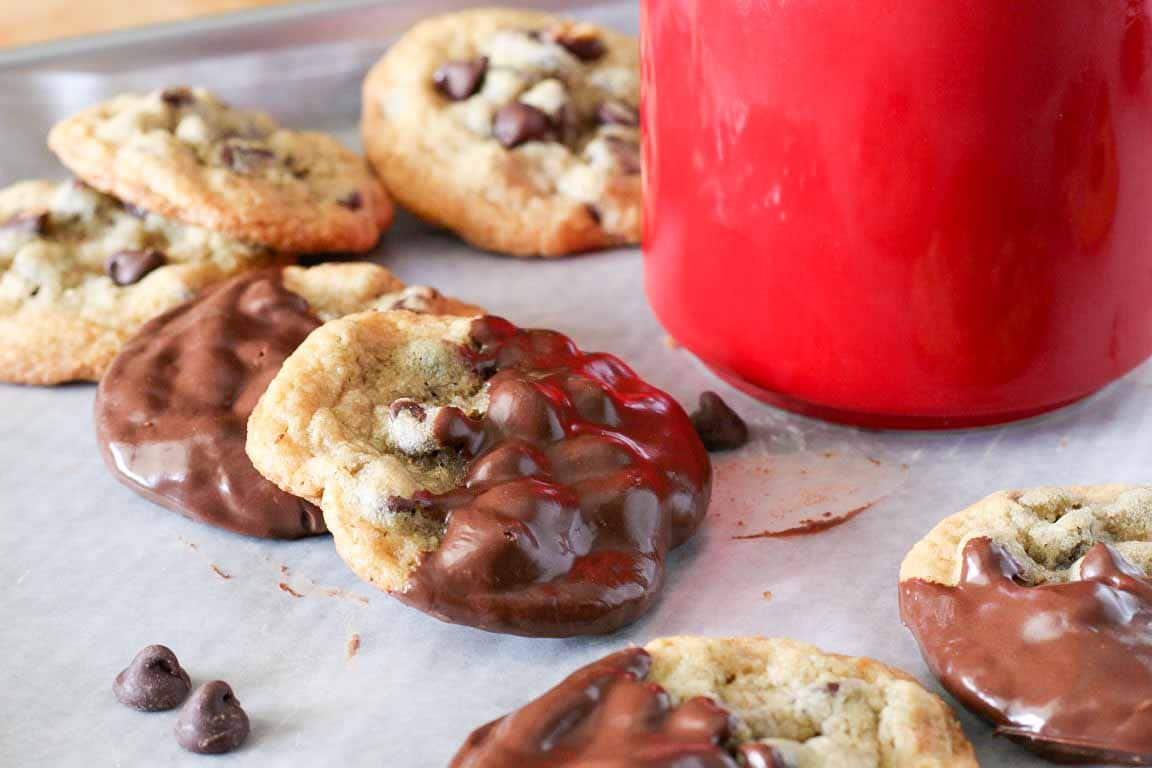 A baking sheet filled with very thin, over-spread chocolate chip cookies with lacy edges, photographed on a kitchen counter