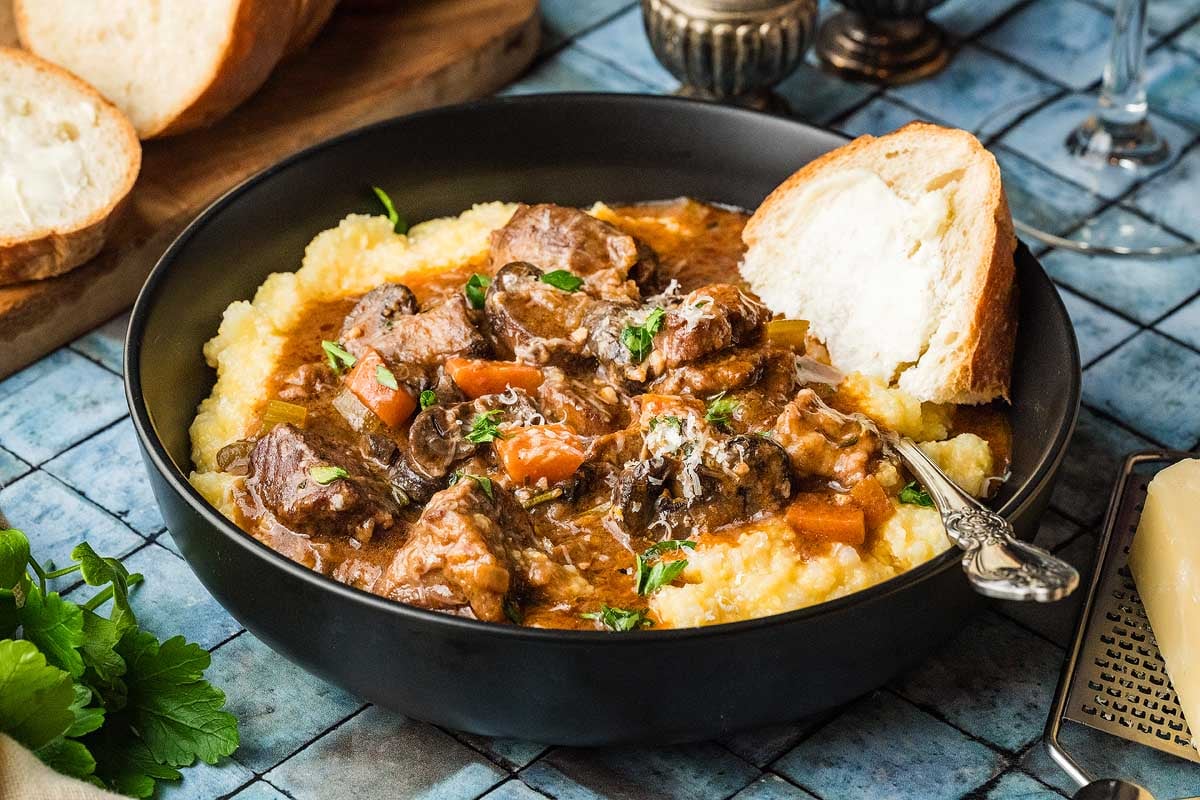 A bowl of beef stew served with a piece of crusty bread on a linen napkin beside the bowl