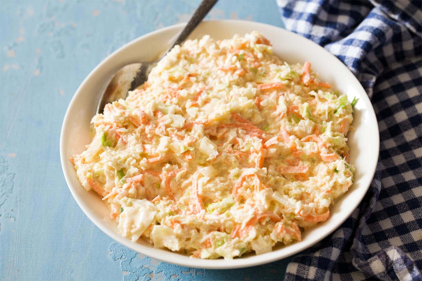 A bowl of creamy coleslaw with very finely chopped cabbage and small flecks of carrot, set on a wooden kitchen table