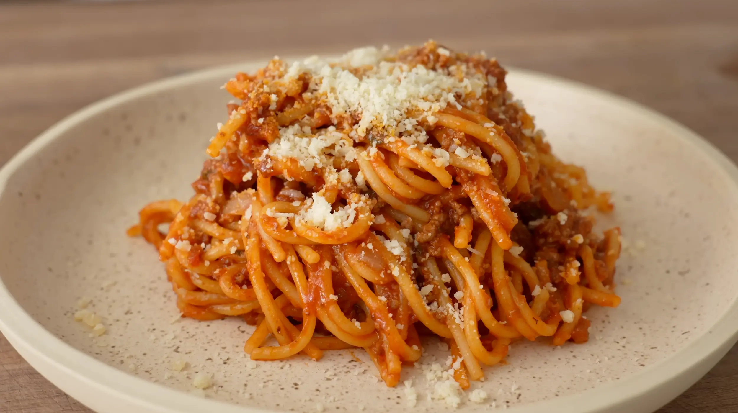 A bowl of spaghetti topped with rich meat sauce and grated Parmesan on a simple dinner table with a fork and napkin