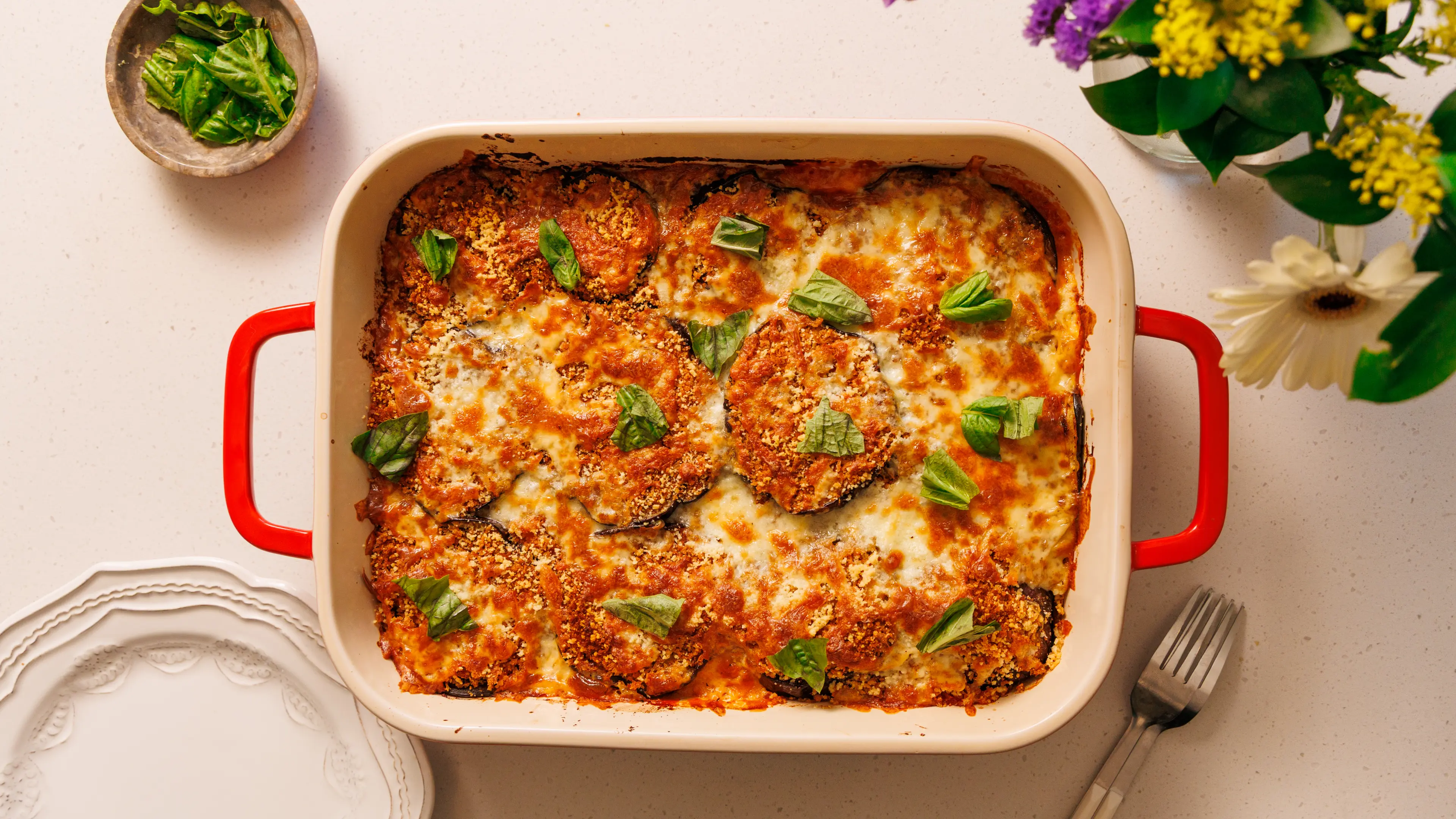 A bubbling baked eggplant parmesan in a rustic casserole dish with browned mozzarella on top, set on a wooden table with a serving spoon