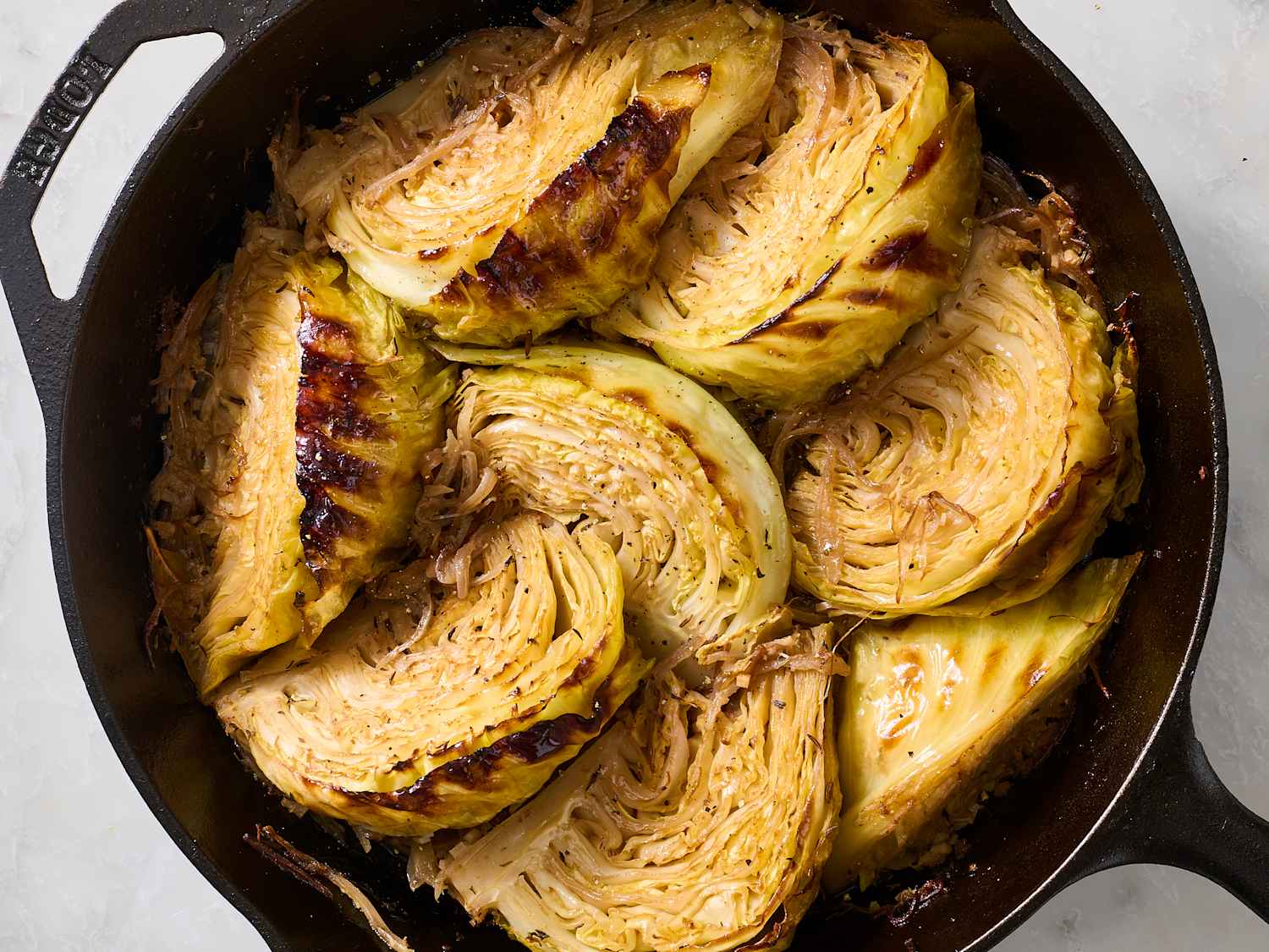 A cast iron skillet filled with deeply caramelized cabbage ribbons with browned edges and glossy sheen, sitting on a stovetop