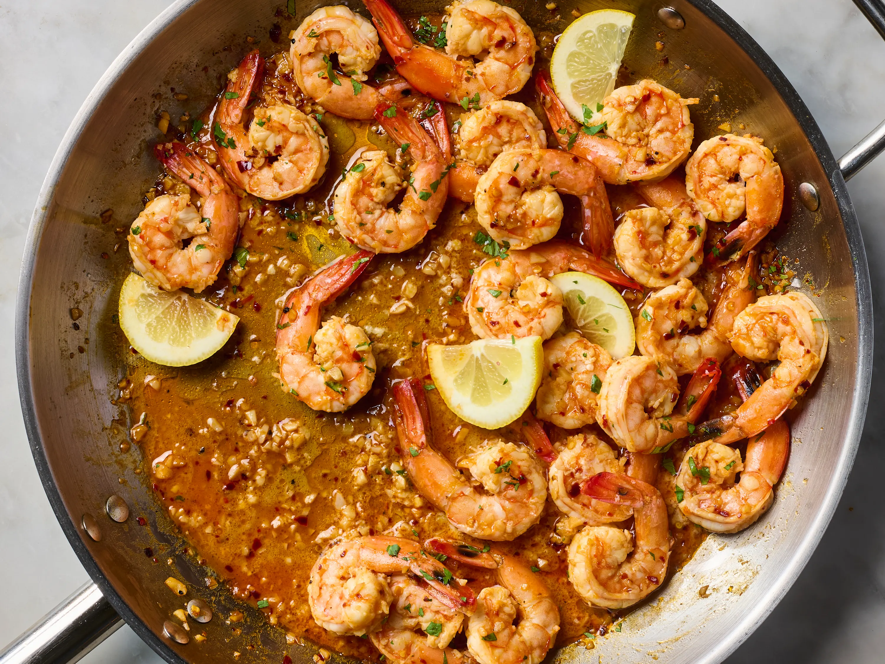 A cast iron skillet of zesty shrimp sizzling with garlic, lemon slices, and herbs on a stovetop
