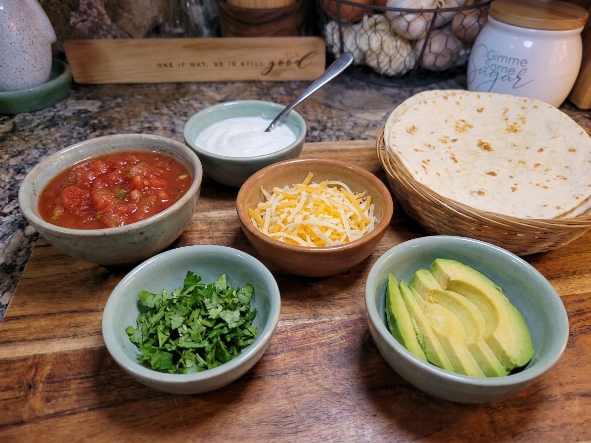 A dinner table setting with small bowls of fajita toppings like salsa, sour cream, shredded cheese, cilantro, and sliced avocado