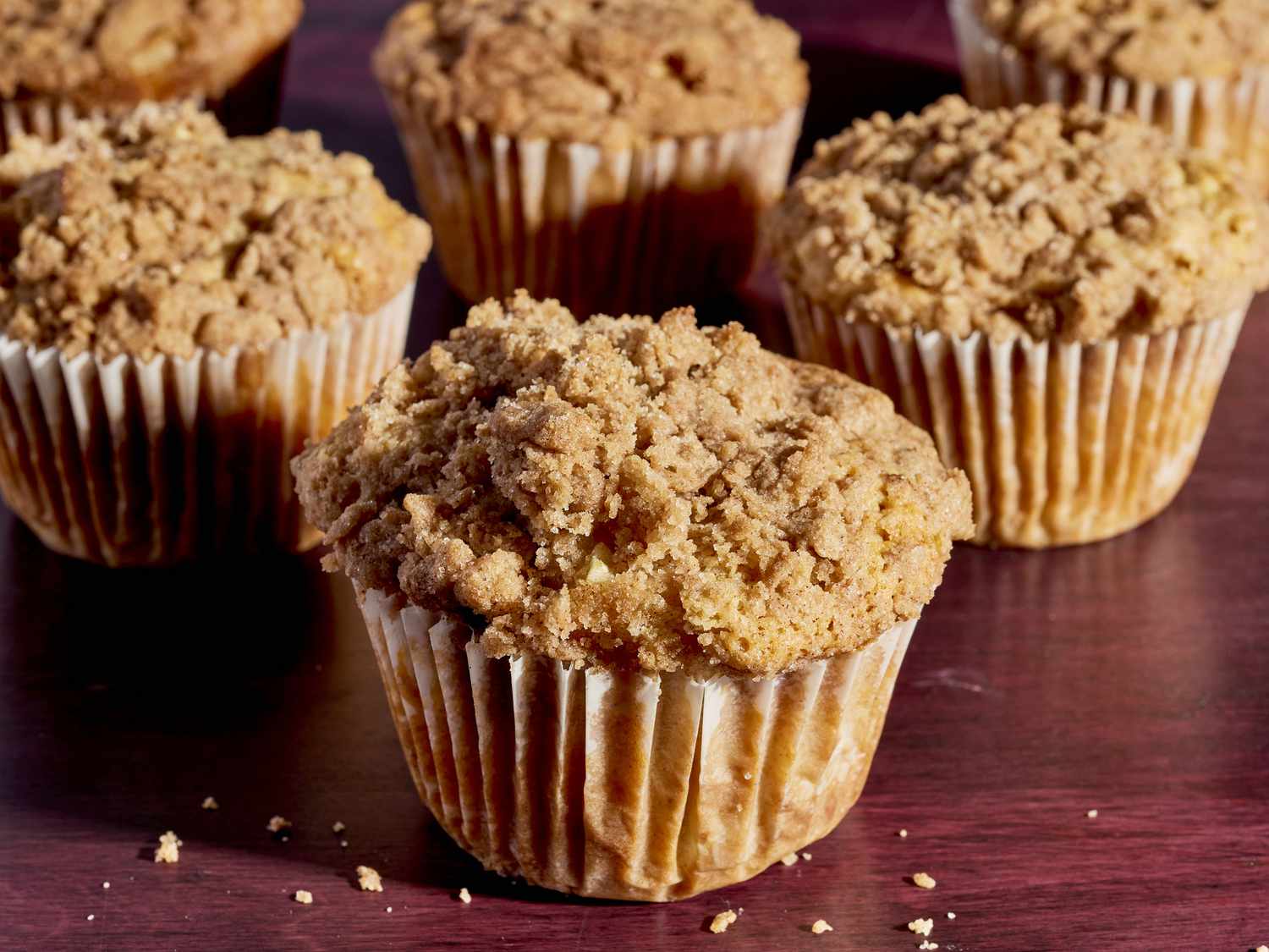 A dozen cinnamon apple muffins cooling on a wire rack on a warm-toned kitchen counter, with visible apple chunks and cinnamon-sugar tops