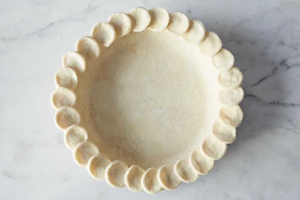 A finished all-butter pie crust in a glass pie dish with deeply golden, flaky edges sitting on a wooden counter