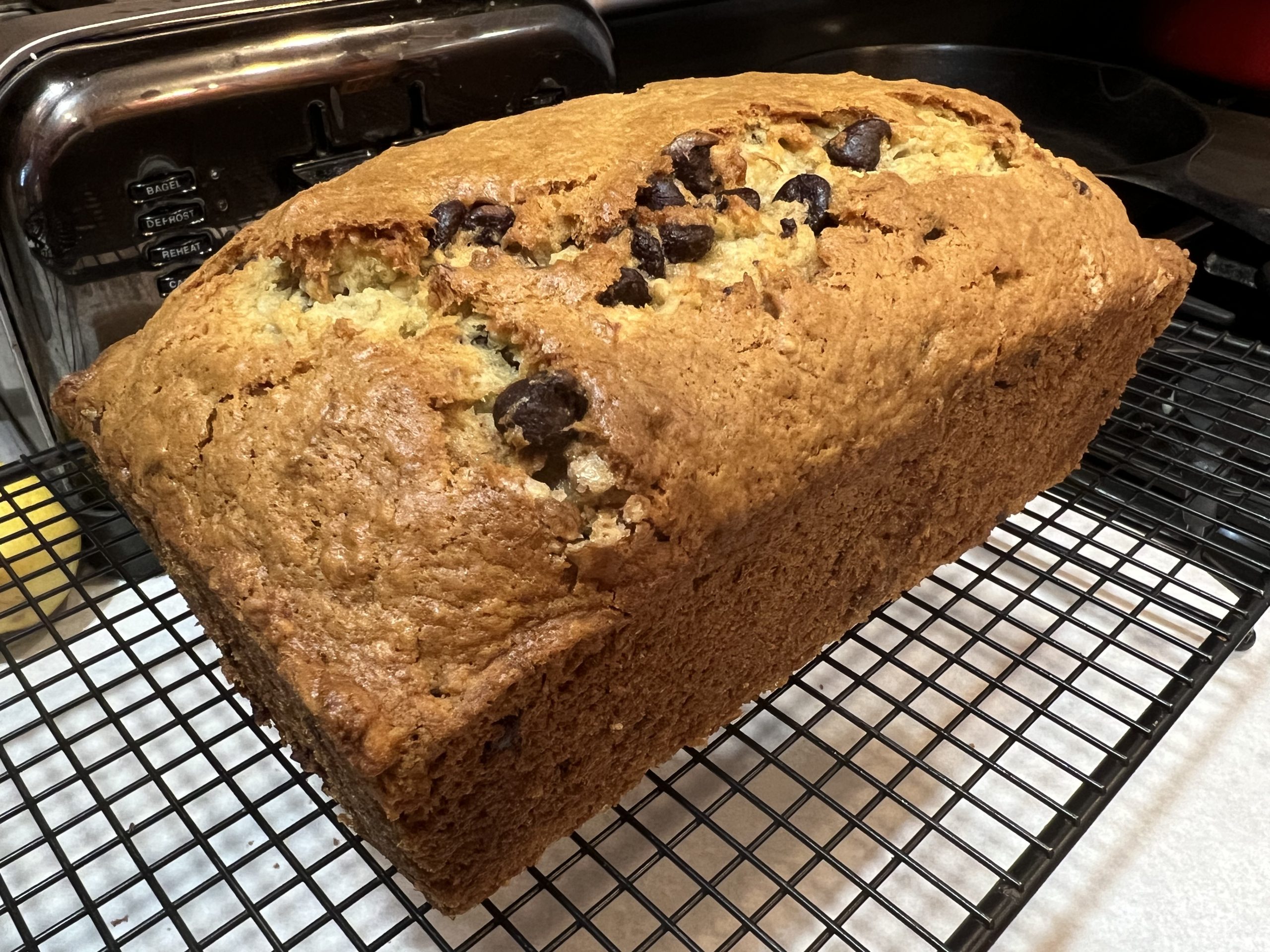 A freshly baked loaf of banana bread cooling on a wire rack on a kitchen counter, with a few banana slices and a butter knife nearby