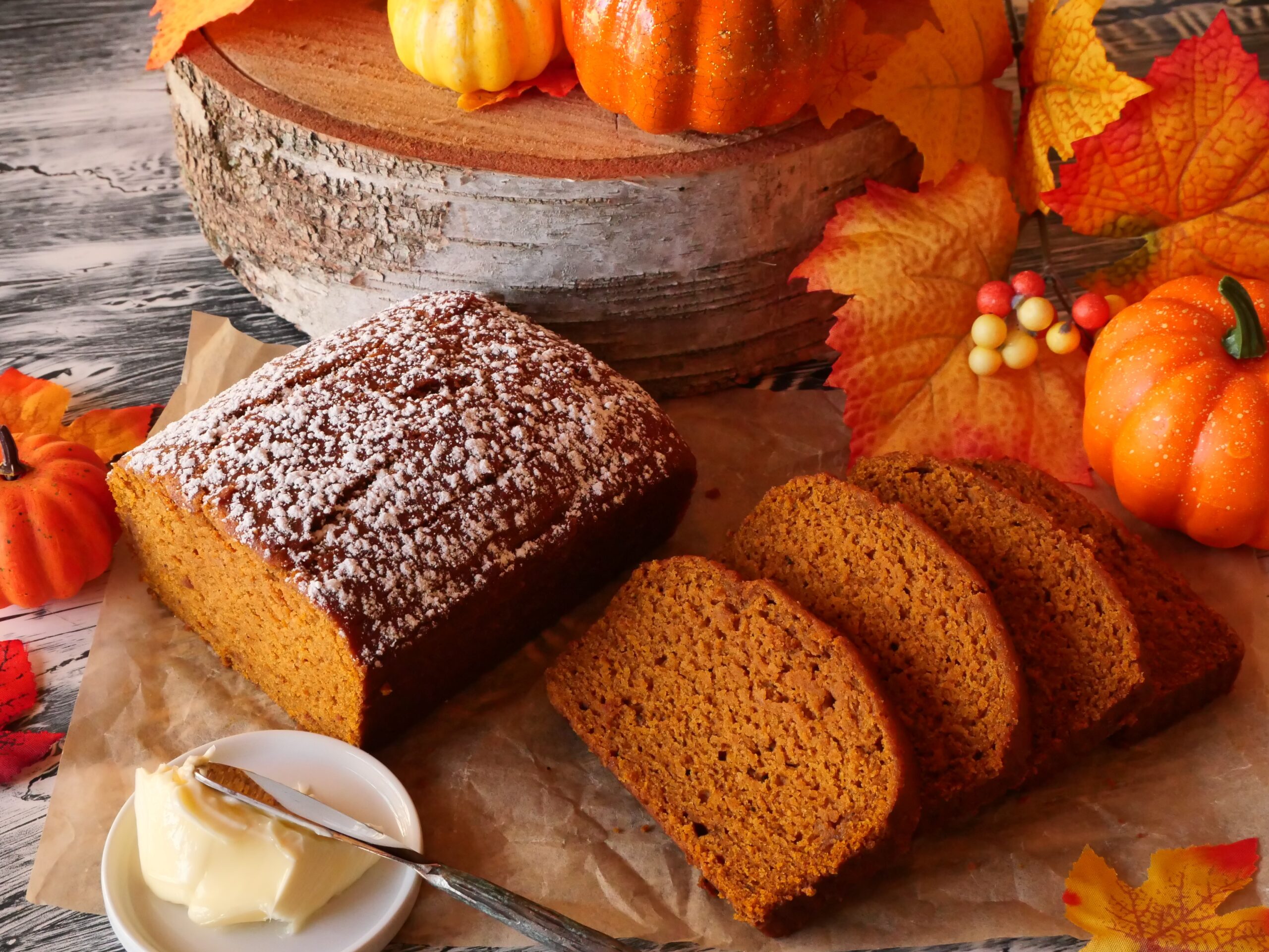 A freshly baked loaf of pumpkin bread on a wooden cutting board with a few slices cut, showing a tender orange crumb
