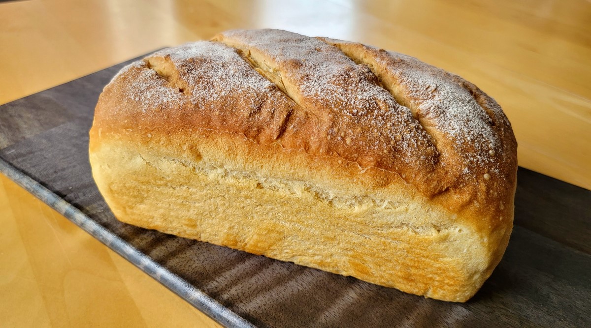 A golden brown homemade yeast bread loaf cooling on a wire rack on a kitchen counter