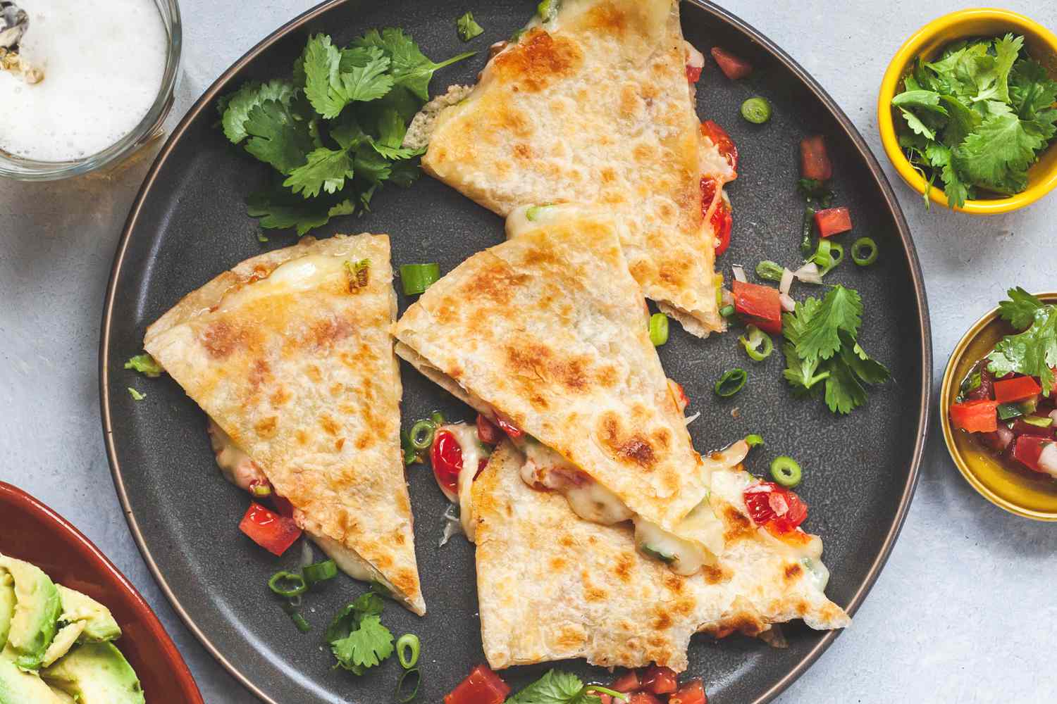 A golden-brown quesadilla cut into wedges on a wooden board with a small bowl of salsa and a lime wedge nearby