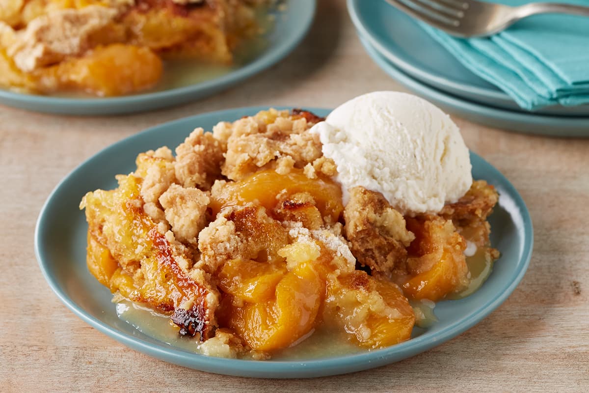 A golden peach cobbler in a baking dish with bubbling peach syrup around the edges and a crisp cake mix topping