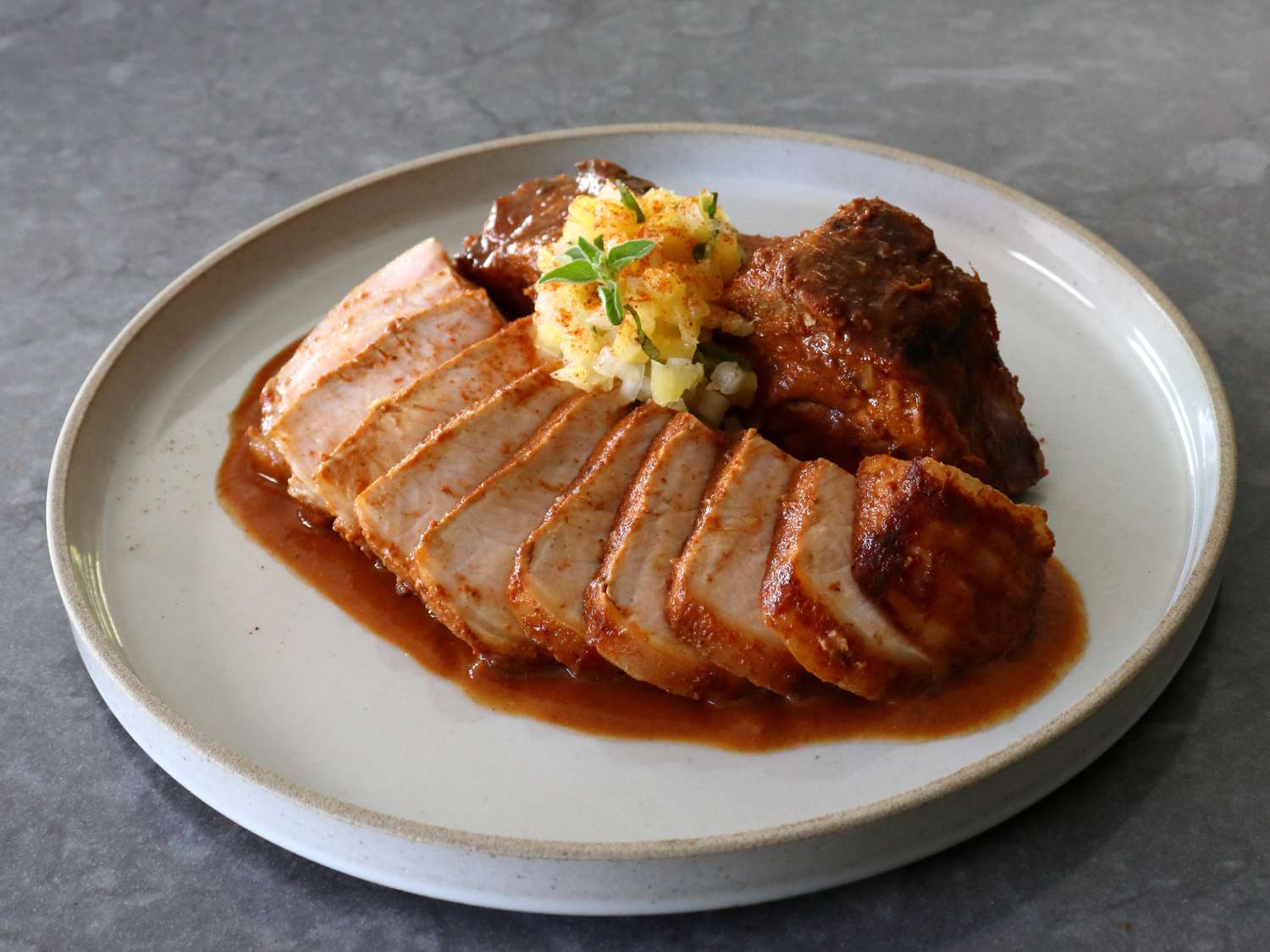 A juicy, golden-brown pork chop sliced and fanned on a dinner plate with a spooned pan sauce, roasted vegetables on the side, and a fork resting on a linen napkin