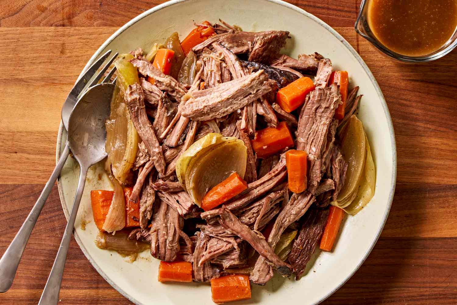 A kitchen counter with a chuck roast, carrots, Yukon gold potatoes, onion, garlic, beef broth, tomato paste, Worcestershire sauce, and dried herbs laid out for pot roast