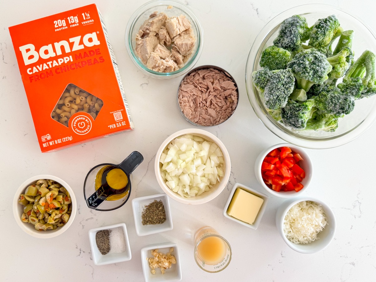 A kitchen counter with shelf-stable pasta dinner ingredients laid out, including dried pasta, canned tomatoes, canned tuna, canned beans, olive oil, garlic, dried herbs, and grated Parmesan