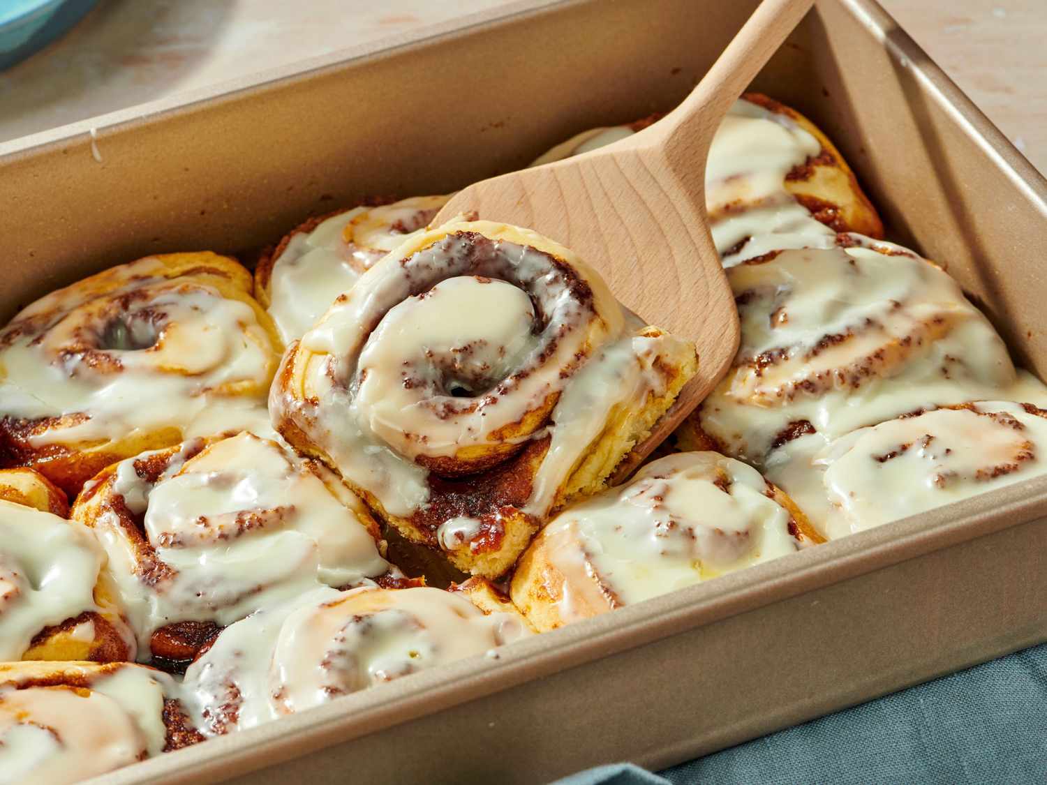 A pan of freshly baked cinnamon rolls with thick vanilla cream cheese icing melting into the spirals on a kitchen counter