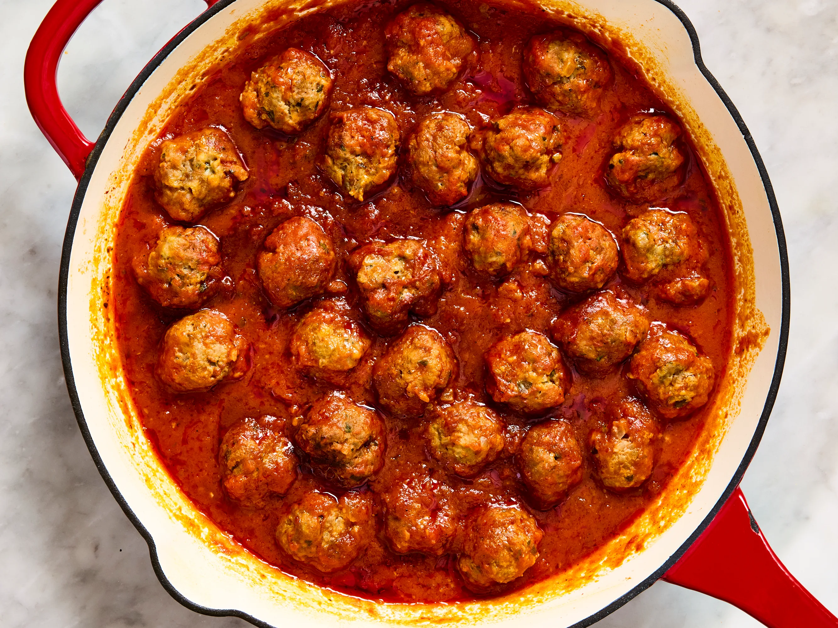 A plate of classic browned meatballs in a shallow bowl with a ladle of marinara sauce, a sprinkle of parsley, and warm kitchen lighting
