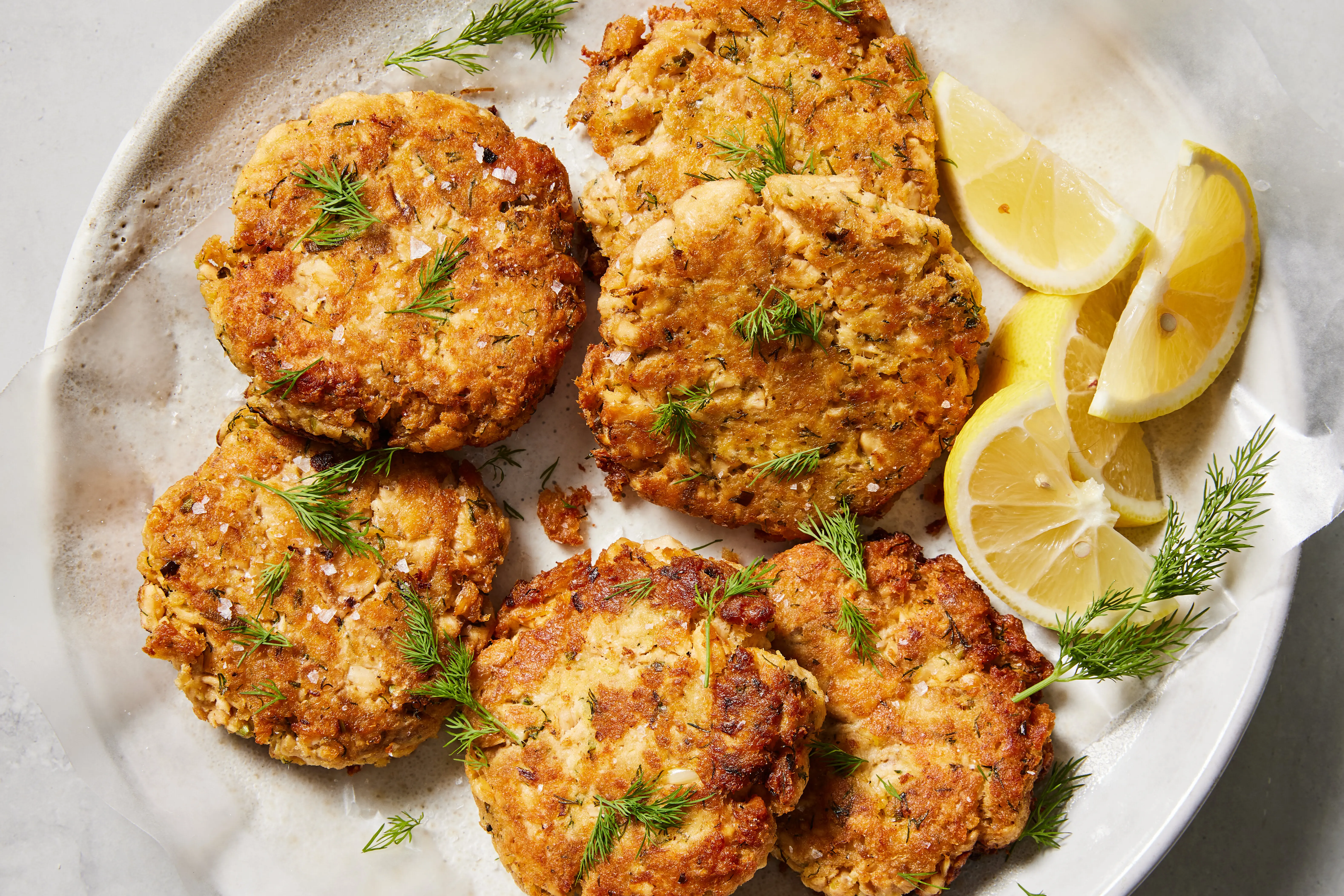 A plate of golden brown salmon patties with a crisp crust, served with lemon wedges and a small bowl of creamy dipping sauce on a wooden table