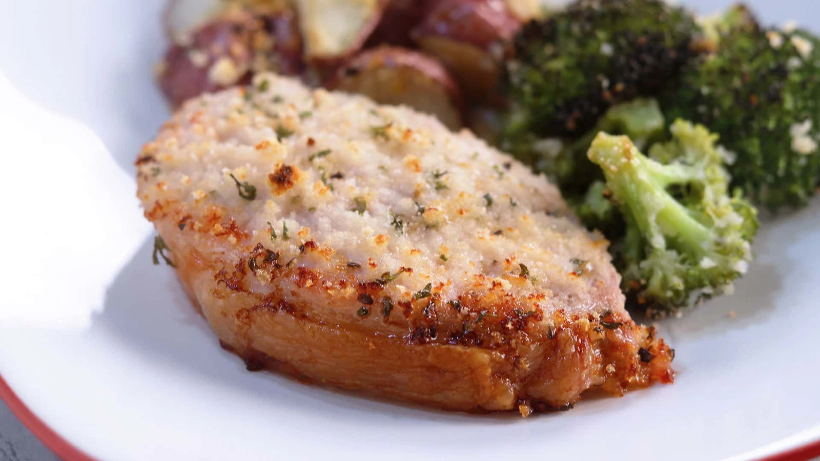 A plate of golden oven-baked pork chops with creamy garlic Parmesan sauce spooned over the top, with parsley scattered and a fork resting nearby