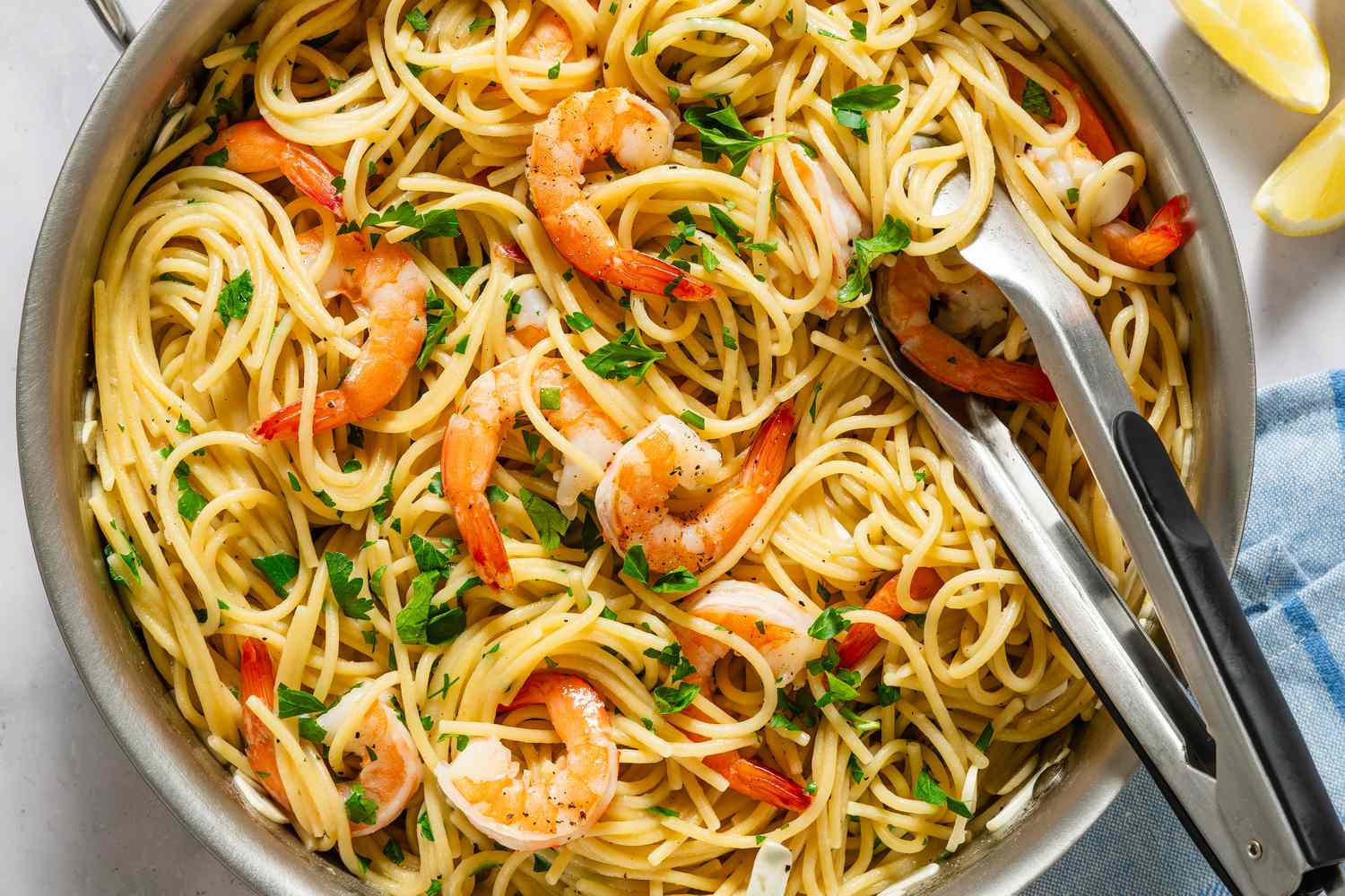 A plate of pasta topped with garlic butter shrimp and parsley, with a lemon wedge on the side