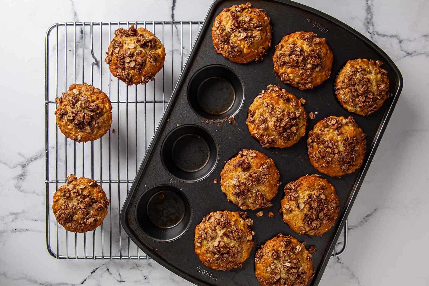 A plate of soft banana oat muffins with golden tops on a wooden kitchen table, with a peeled ripe banana and a small bowl of oats nearby
