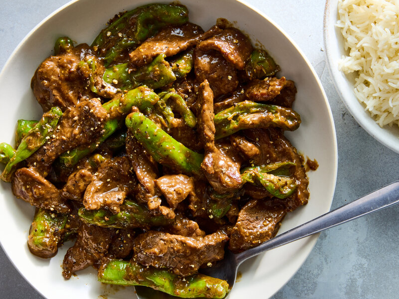 A plated bowl of smoky spicy beef stir fry with glossy slices of beef, red bell peppers, and broccoli, garnished with sesame seeds and sliced scallions
