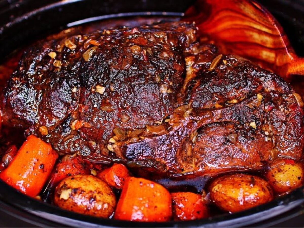 A plated crock pot pork roast sliced and fanned on a serving platter with carrots and potatoes, glossy gravy spooned over the top, warm dinner table setting