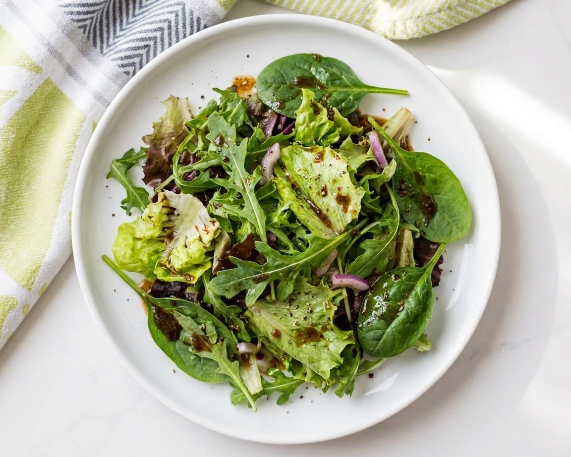 A plated mixed green salad lightly dressed with balsamic vinaigrette on a white ceramic plate