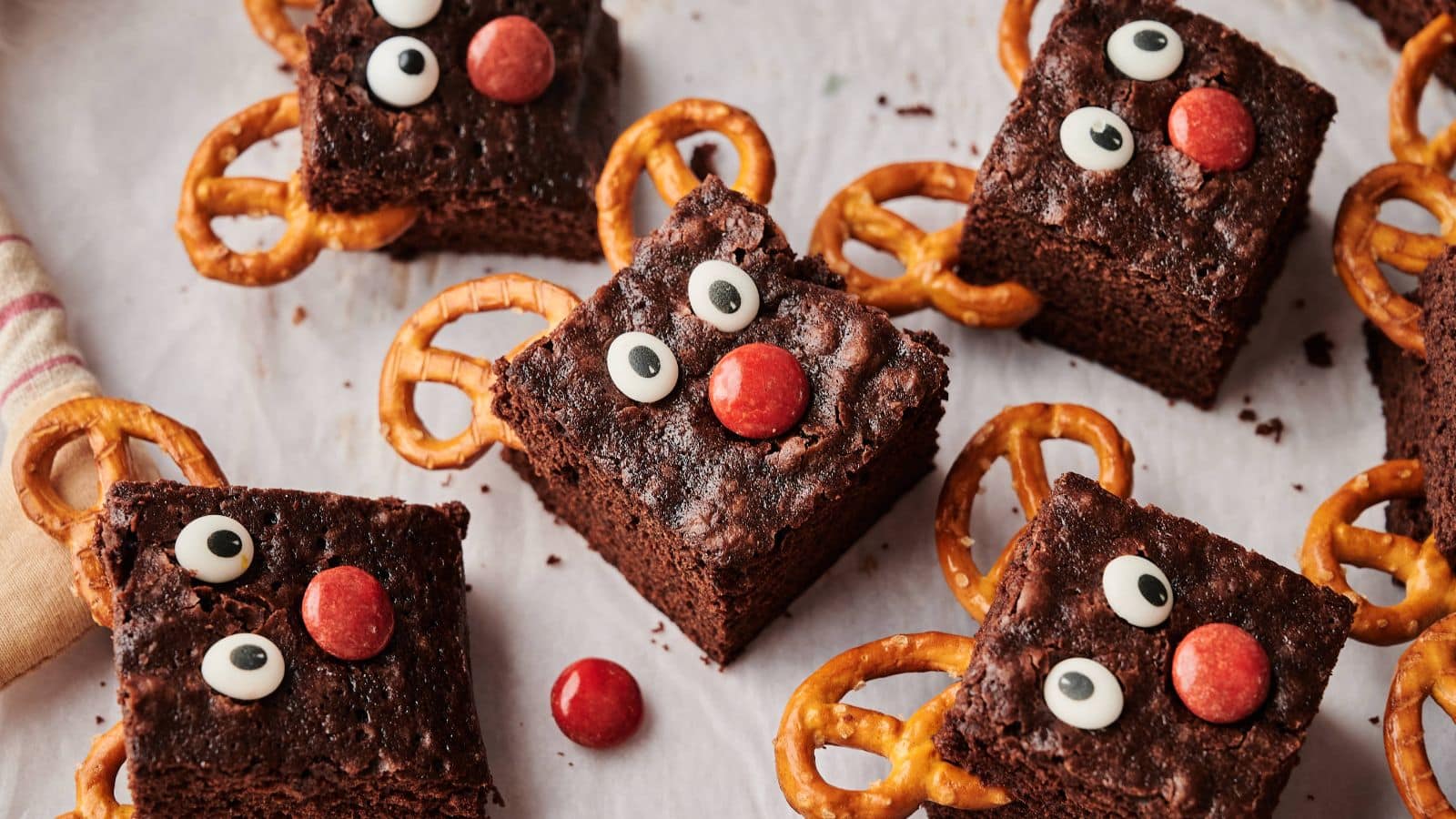 A platter of glossy-topped chocolate brownies cut into neat squares on a holiday table with twinkle lights in the background