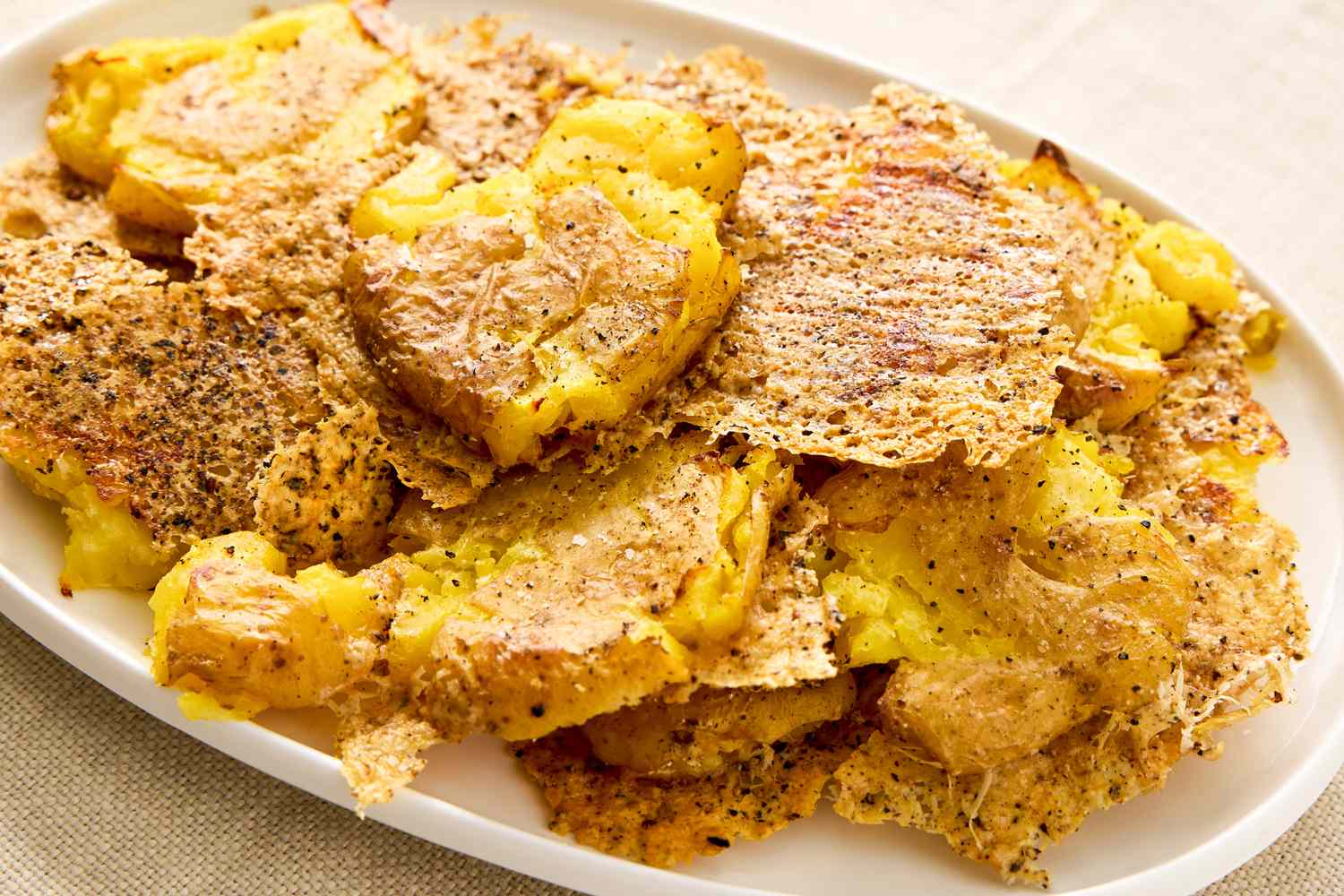 A platter of golden smashed potatoes with crisp edges and melted Parmesan, sprinkled with chopped parsley on a rustic wooden table