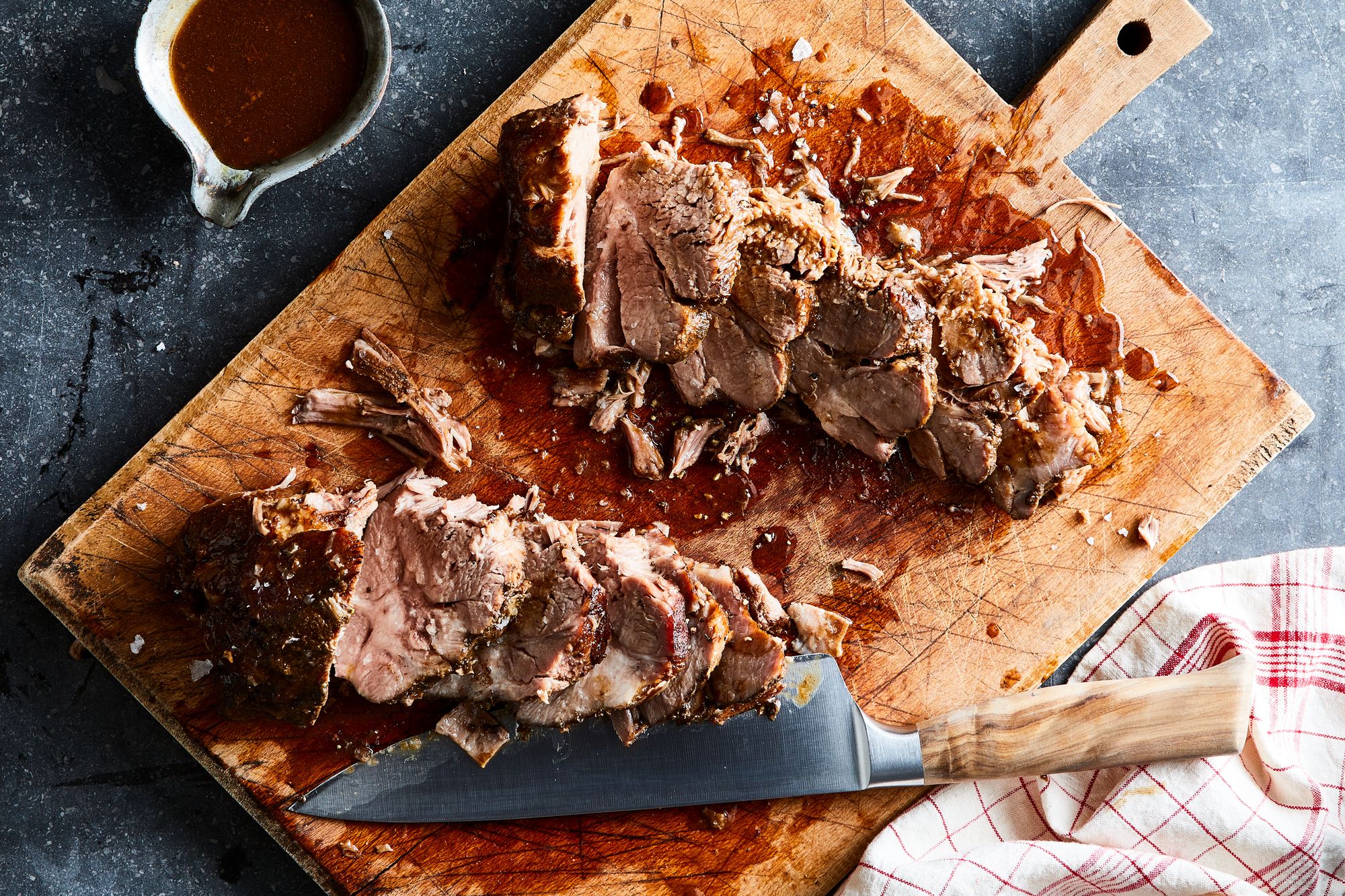 A pork shoulder coated in spice rub sitting in a slow cooker insert with sliced onions underneath