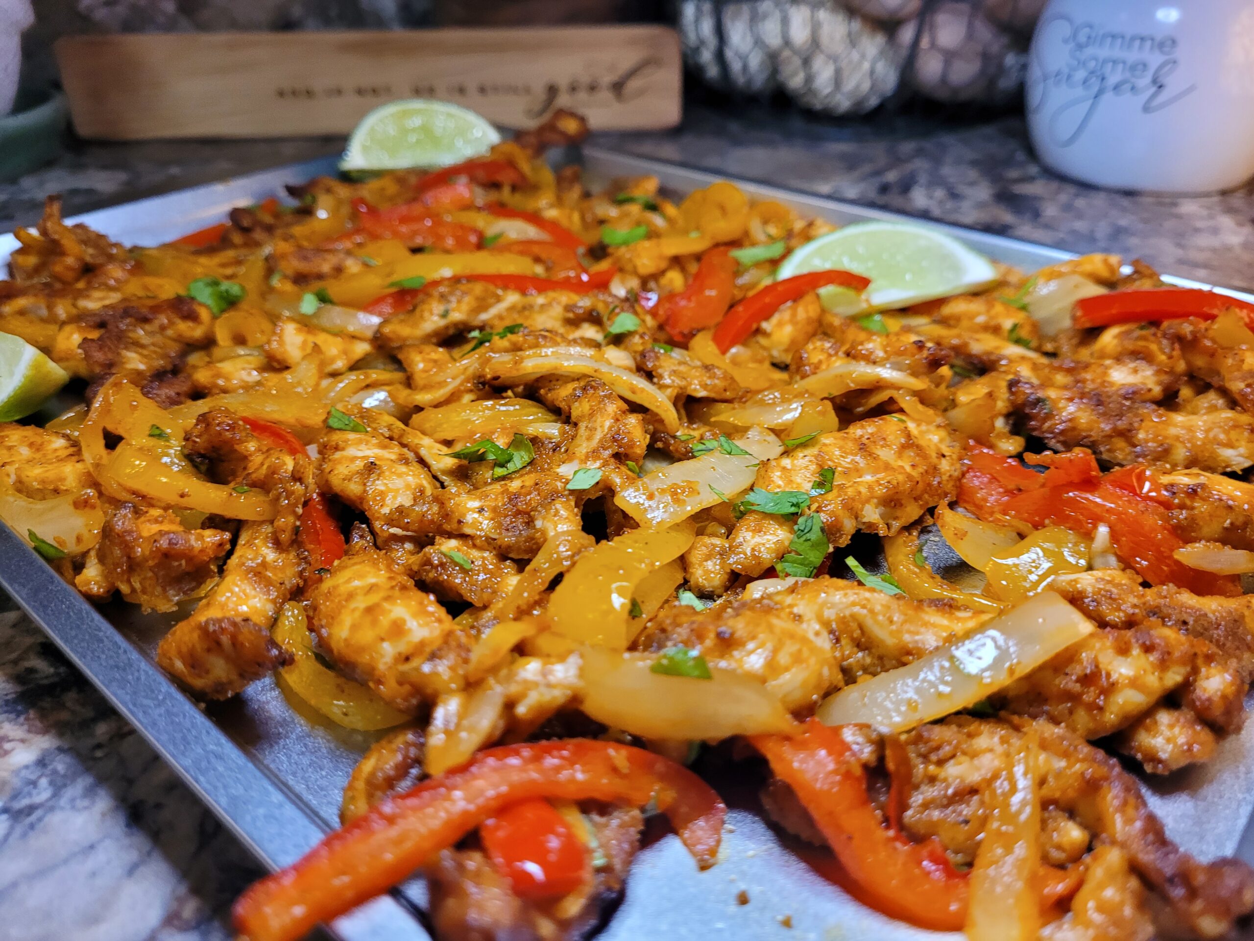 A rimmed sheet pan filled with sliced chicken, red and green bell peppers, and onion strips roasted until lightly charred at the edges