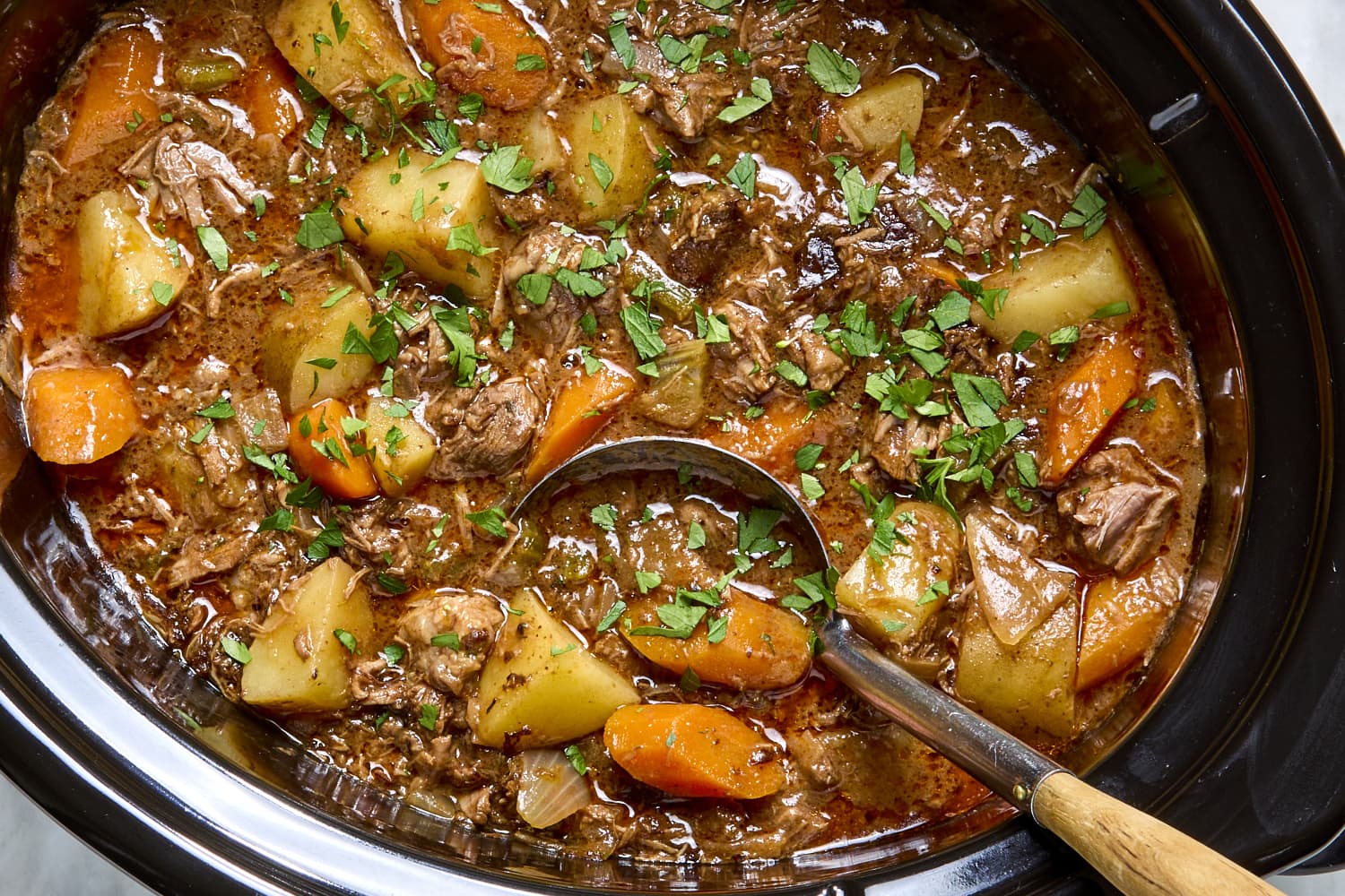 A single bowl of slow cooker beef and vegetable stew with tender beef chunks, potatoes, carrots, and a glossy brown broth on a rustic wooden table
