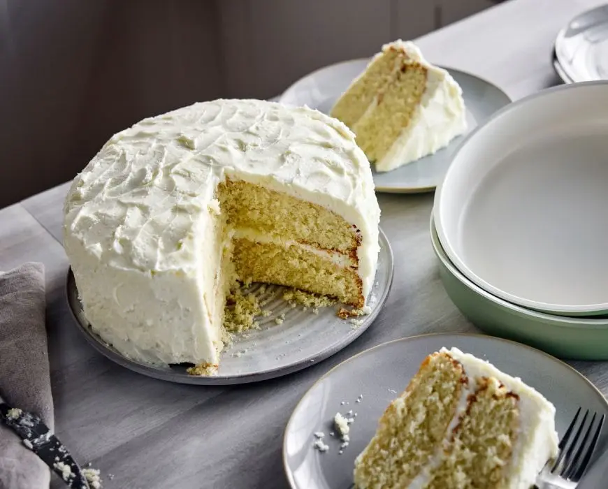 A single frosted vanilla cake on a cake stand with ultra-smooth buttercream and clean, sharp edges in a bright home kitchen