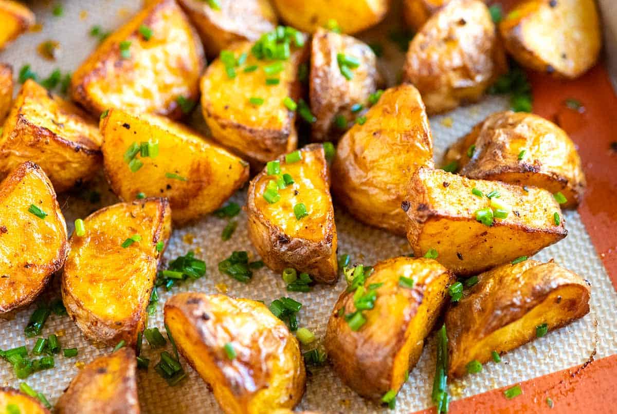 A single sheet pan of crispy roasted potato chunks, deeply golden with browned edges, scattered with chopped parsley and flaky salt on a kitchen counter