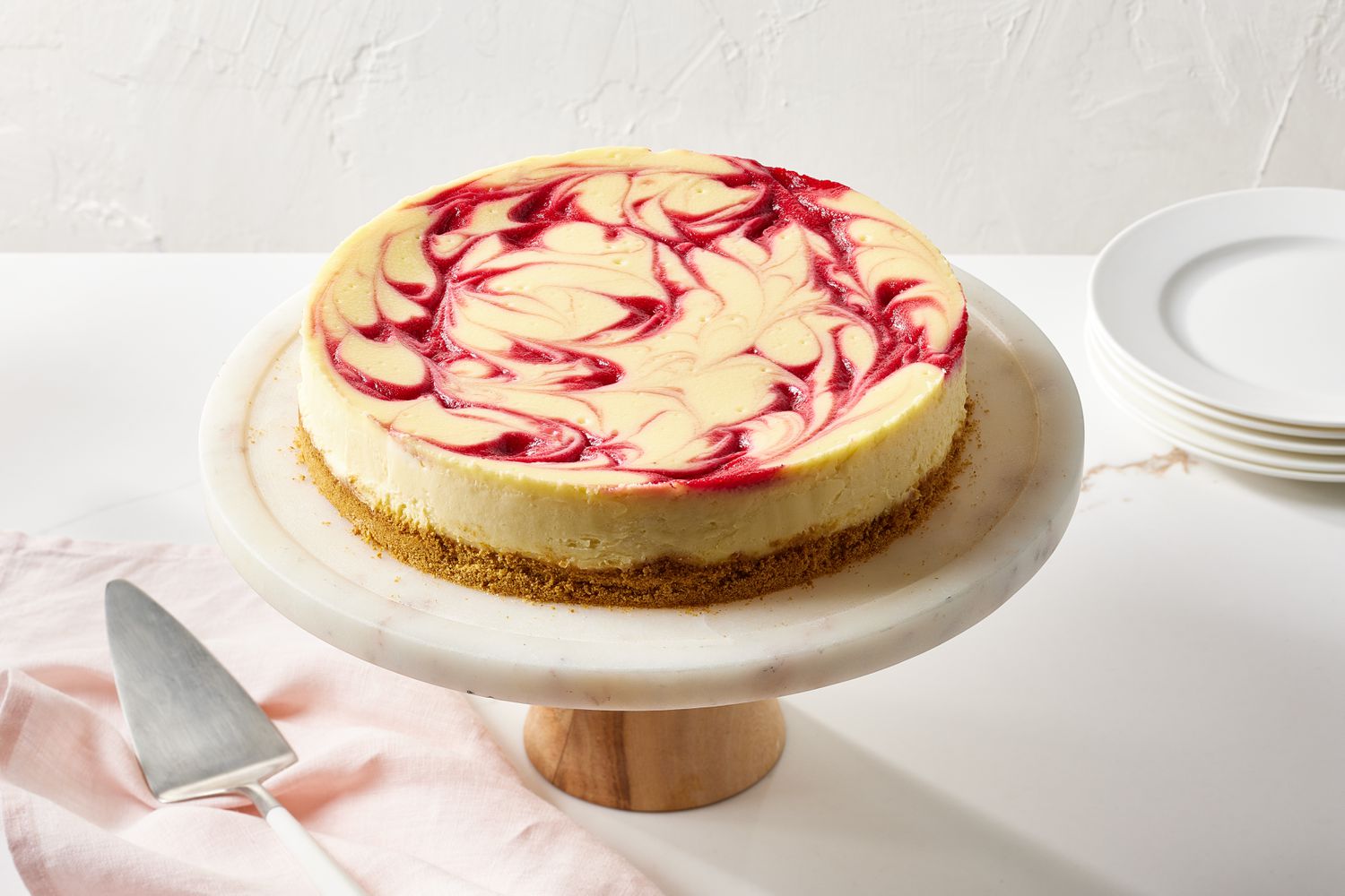 A single slice of raspberry swirl cheesecake on a small dessert plate, showing a creamy ivory filling with vivid raspberry ribbons and a graham cracker crust