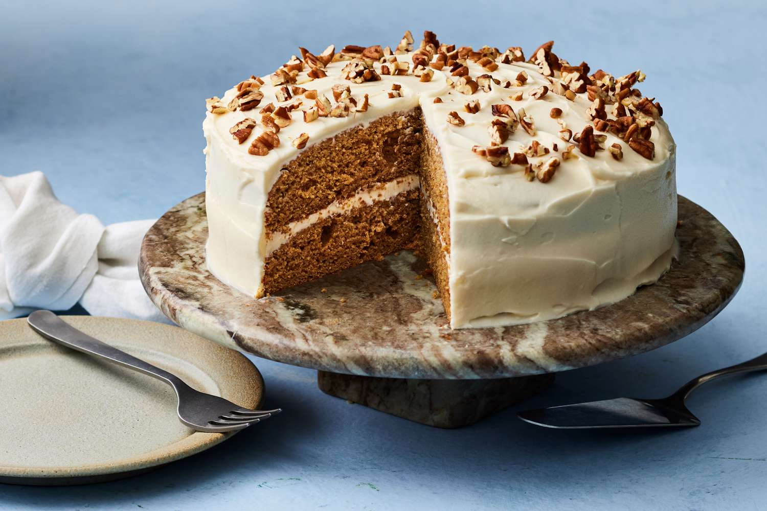 A slice of sweet potato cake on a small plate with a thick layer of cream cheese frosting and a light sprinkle of cinnamon, set on a cozy kitchen table