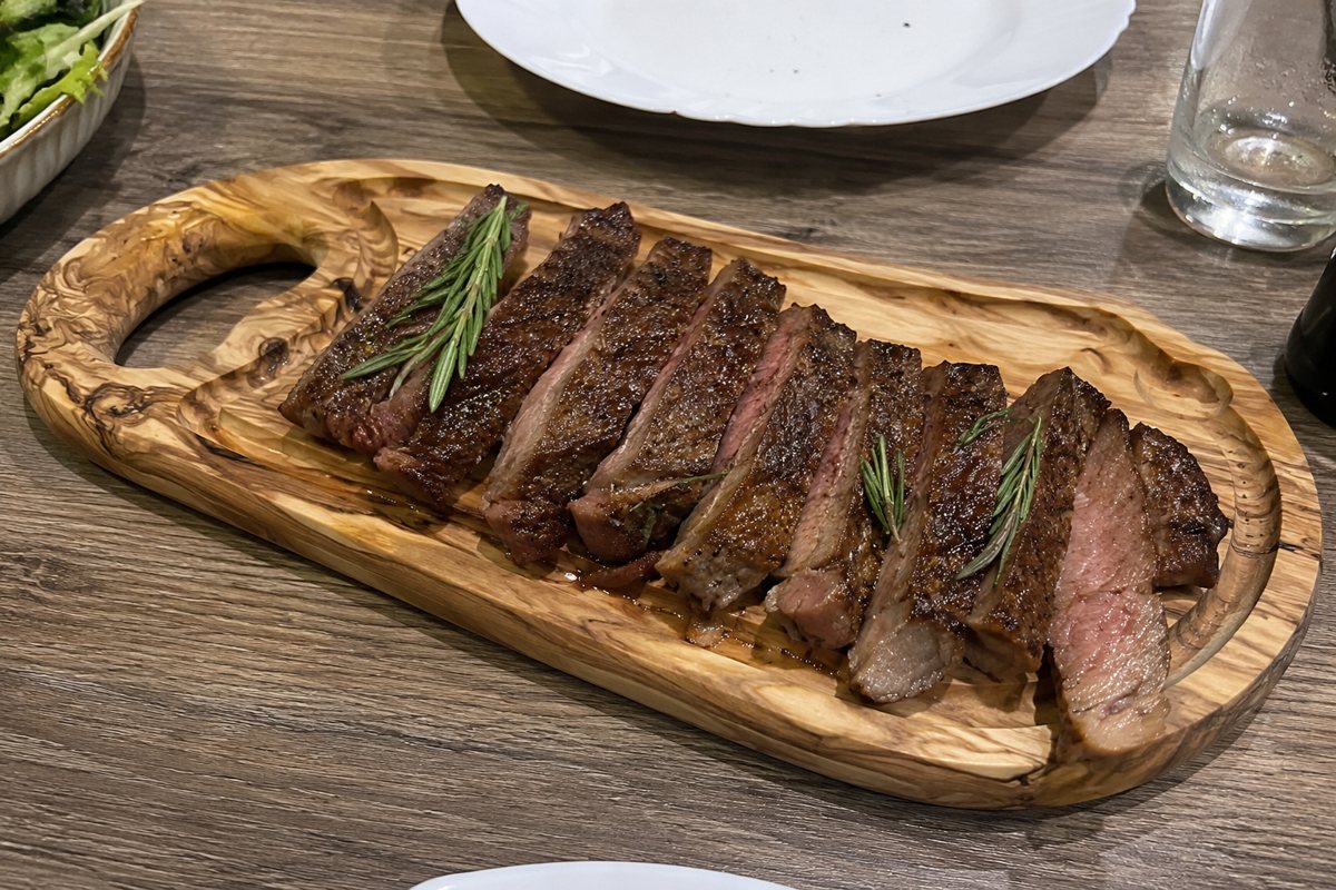 A sliced, medium-rare steak on a cutting board with a browned crust and juices resting nearby, photographed on a weeknight kitchen counter