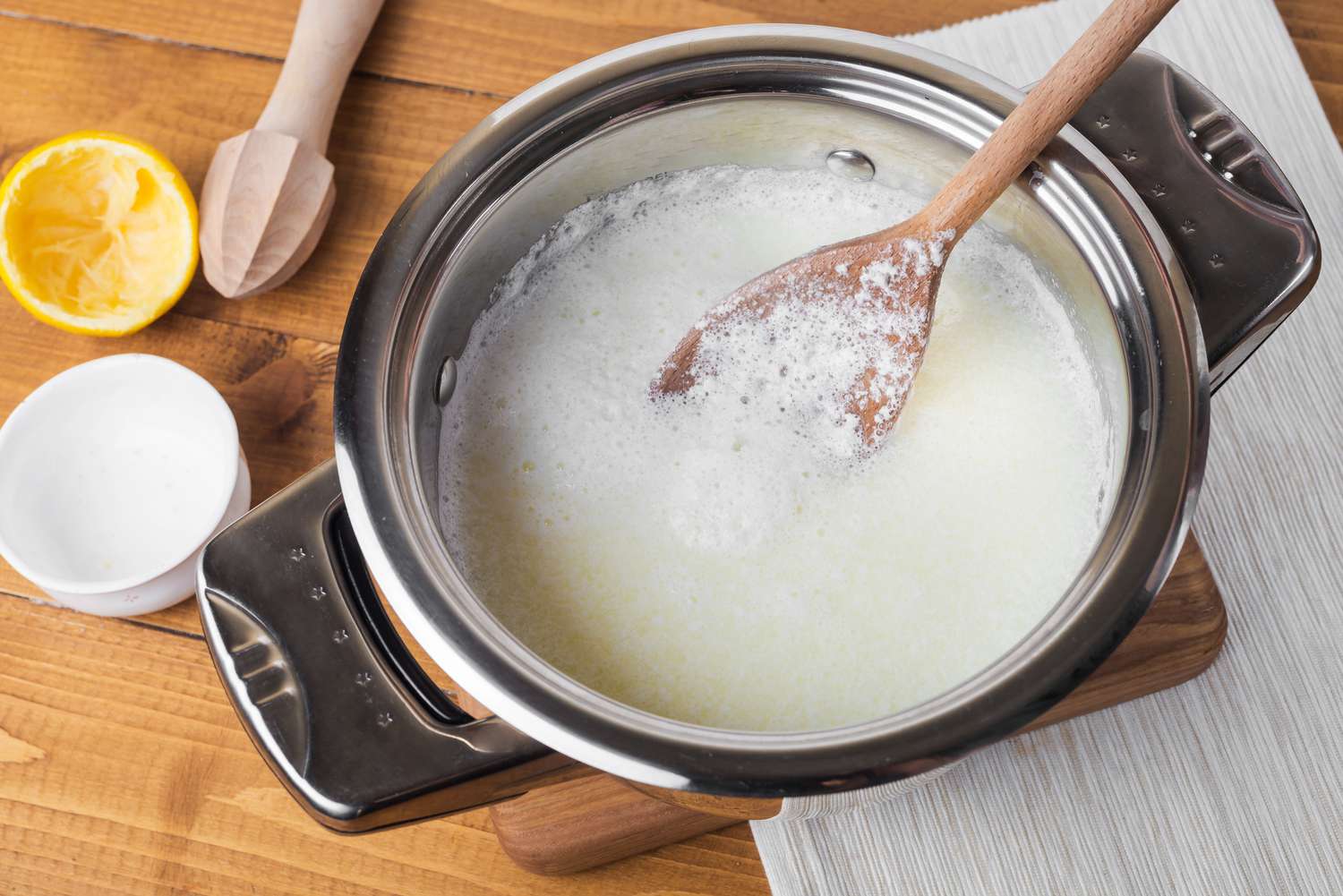 A small bowl of milk with fresh lemon juice being whisked in on a home kitchen counter, with a measuring spoon and halved lemon nearby