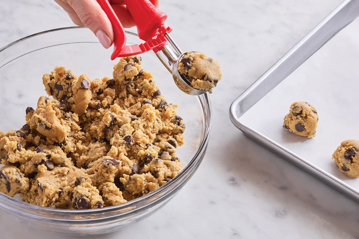 A small cookie scoop portioning chocolate chip cookie dough onto a parchment-lined baking sheet