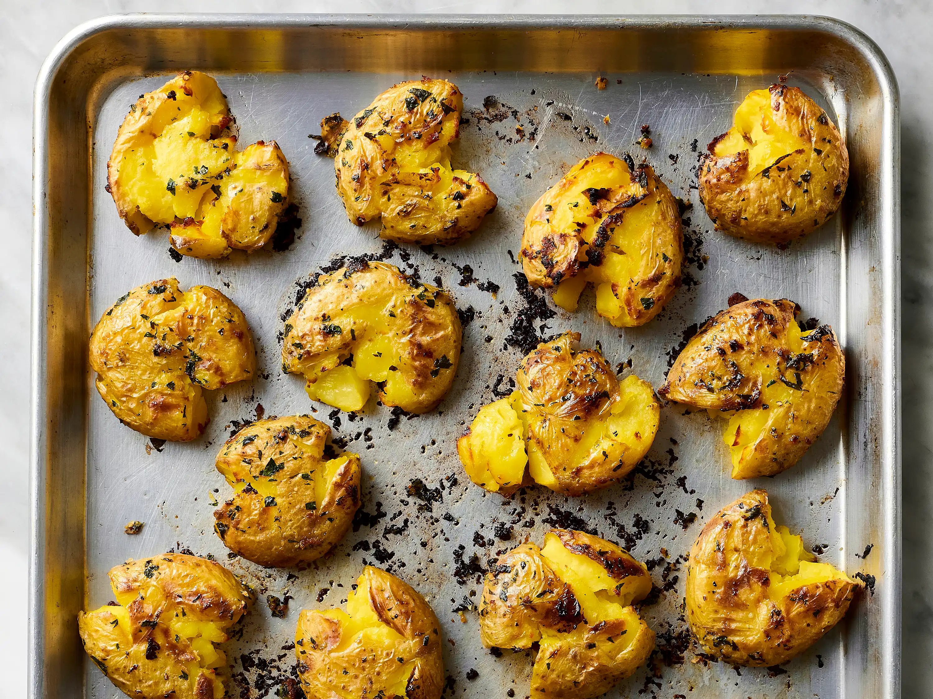 A split baked russet potato on a white plate with a pat of butter melting into the fluffy interior and a sprinkle of flaky salt, warm kitchen lighting