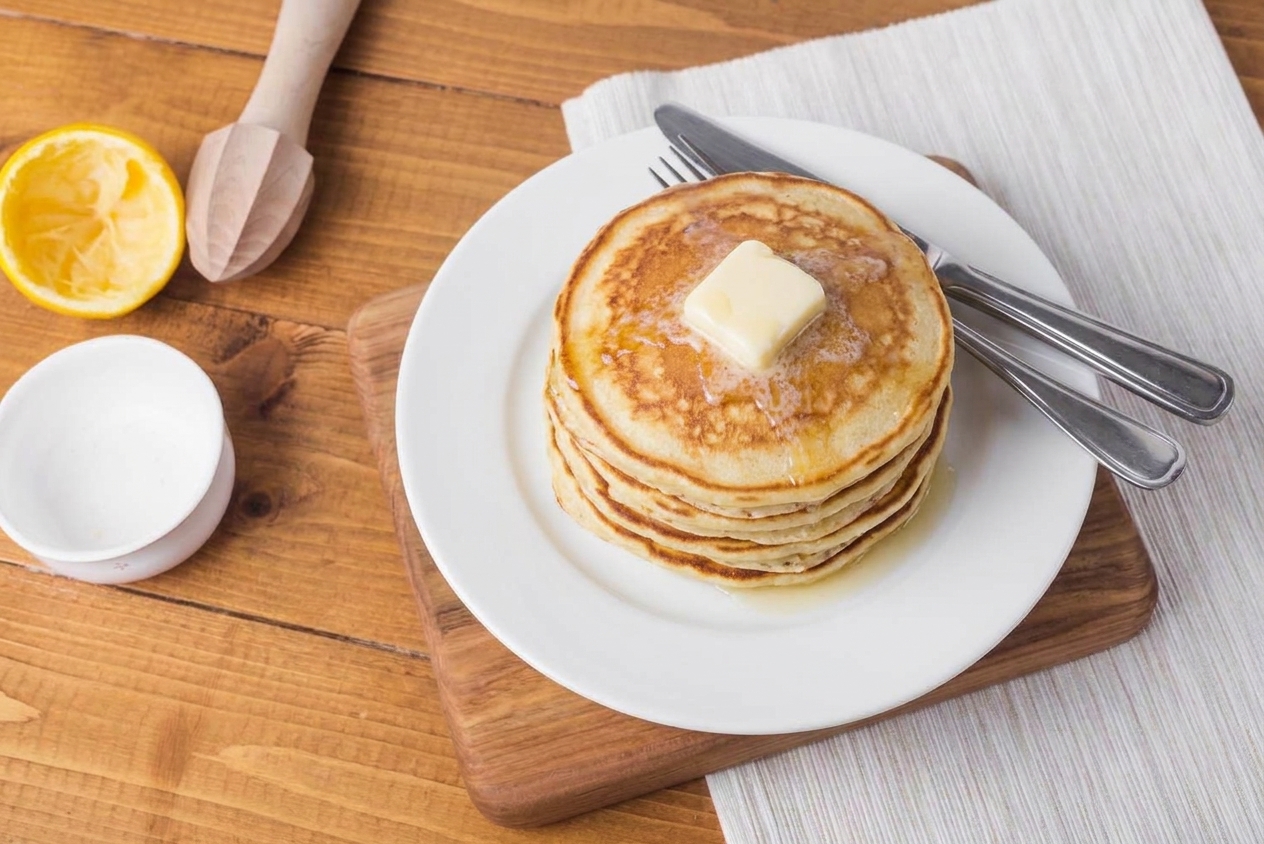 A stack of fluffy pancakes on a ceramic plate with a pat of butter melting on top, set on a breakfast table
