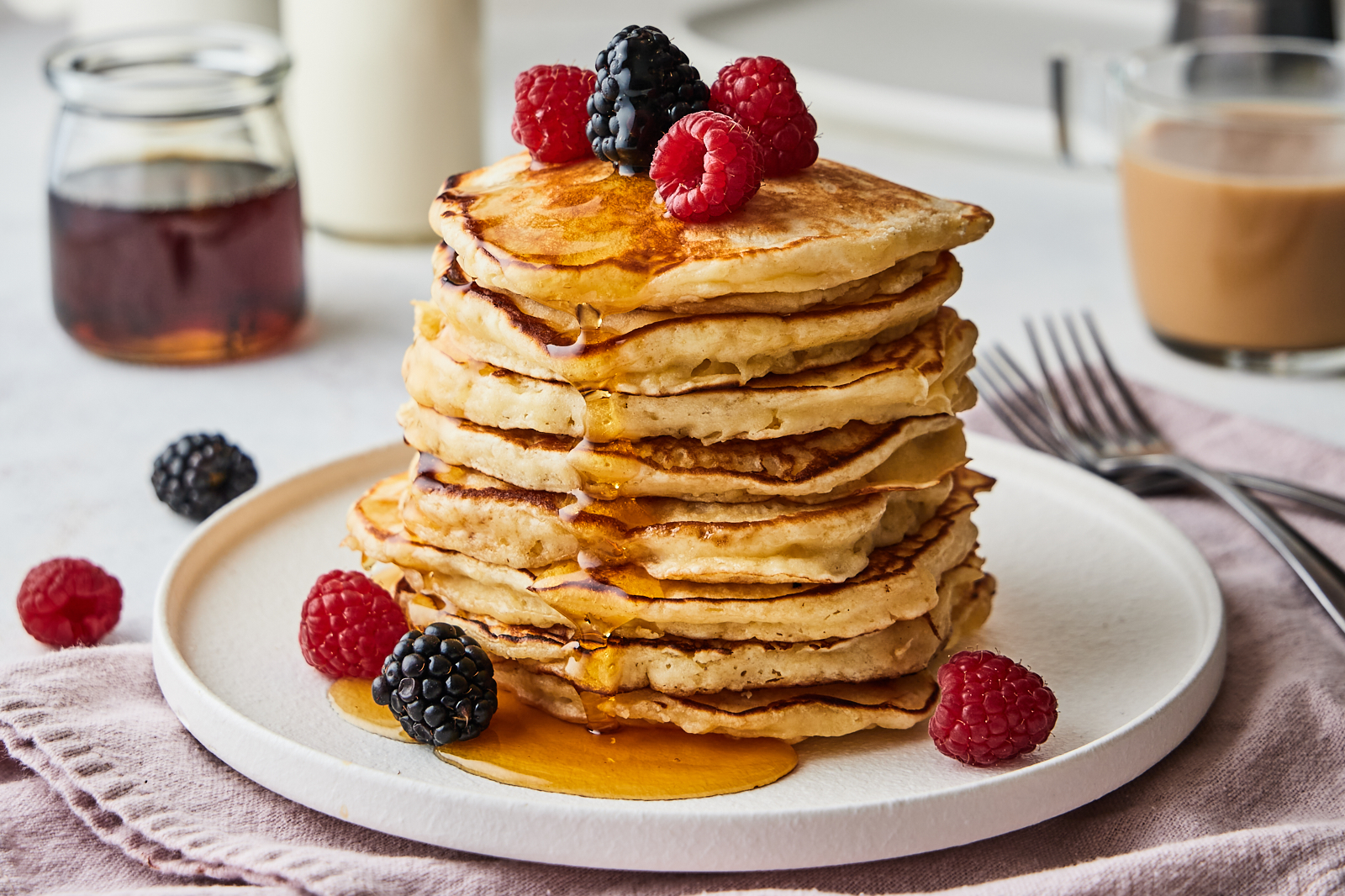 A stack of light and fluffy pancakes on a ceramic plate with a pat of butter melting on top and maple syrup drizzled down the sides