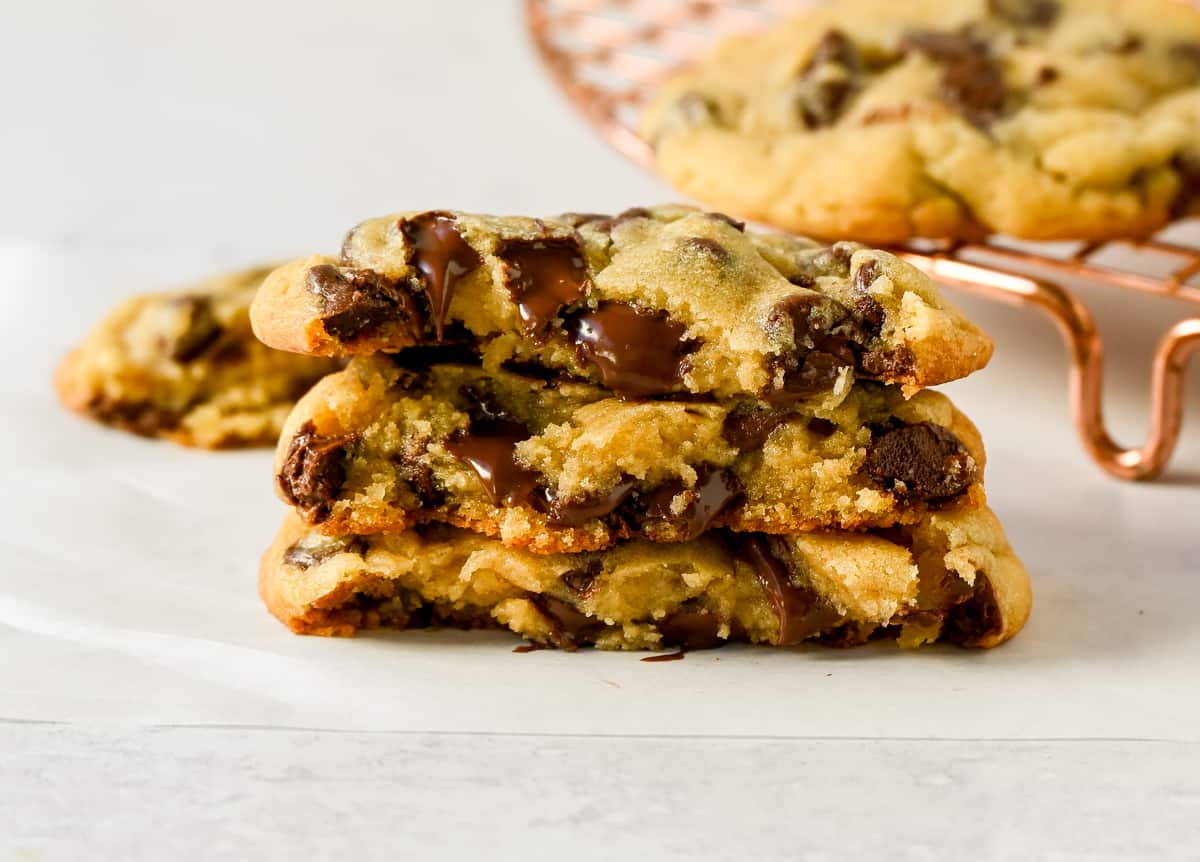 A stack of warm Toll House-style chocolate chip cookies with glossy melted chocolate pockets on a parchment-lined plate