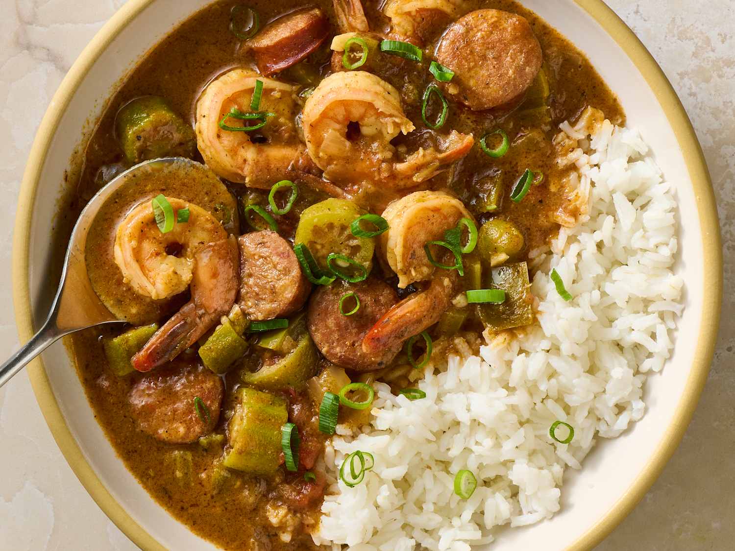 A steaming bowl of shrimp gumbo served over white rice, with visible shrimp, okra, and a glossy dark broth in a rustic ceramic bowl