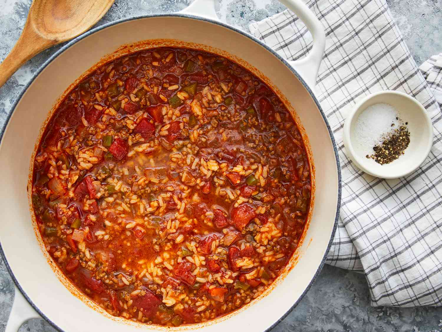 A steaming bowl of stuffed pepper soup with ground beef, diced bell peppers, rice, and a sprinkle of parsley on top on a wooden table