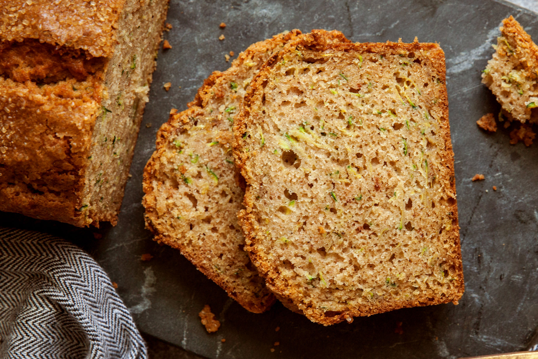 A thick-sliced loaf of moist zucchini bread on a wooden cutting board with visible green zucchini flecks and a golden brown crust