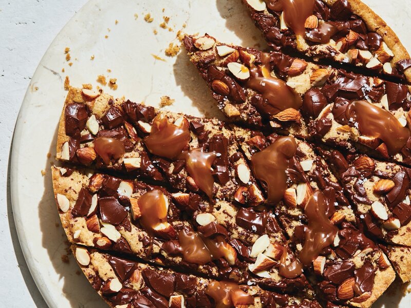 A thick spiced chocolate chip cookie cake baked in a round pan, sliced into wedges with melted chocolate chips visible and lightly golden edges