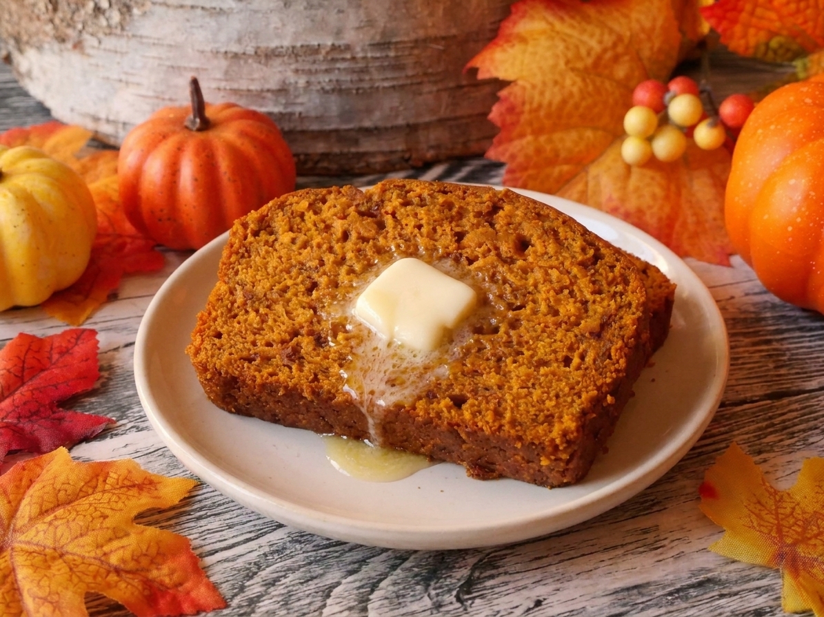 A toasted slice of pumpkin bread on a small plate with a pat of butter melting on top, set on a wooden table