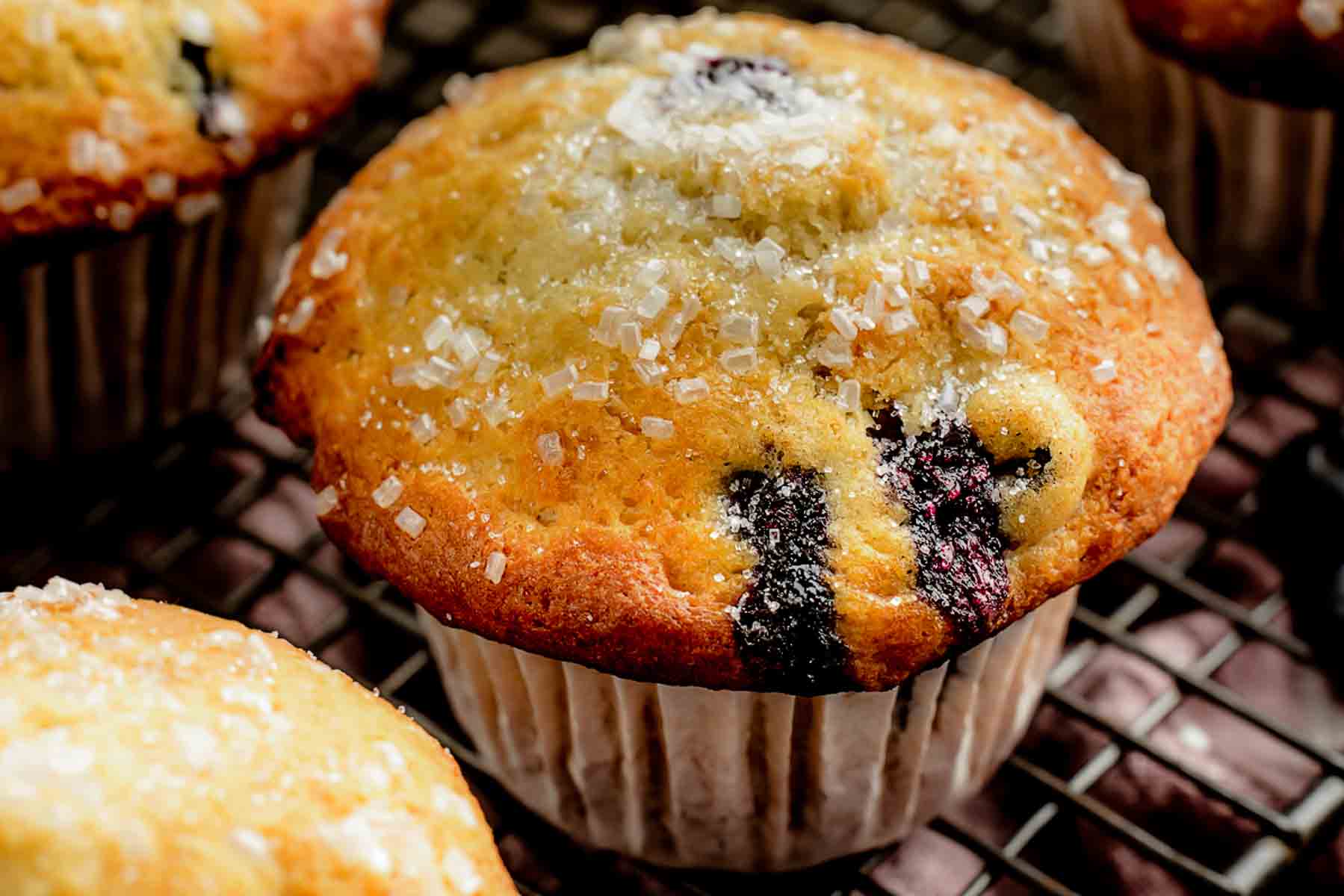 Freshly baked blueberry muffins cooling on a wire rack on a kitchen counter, with a muffin tin nearby