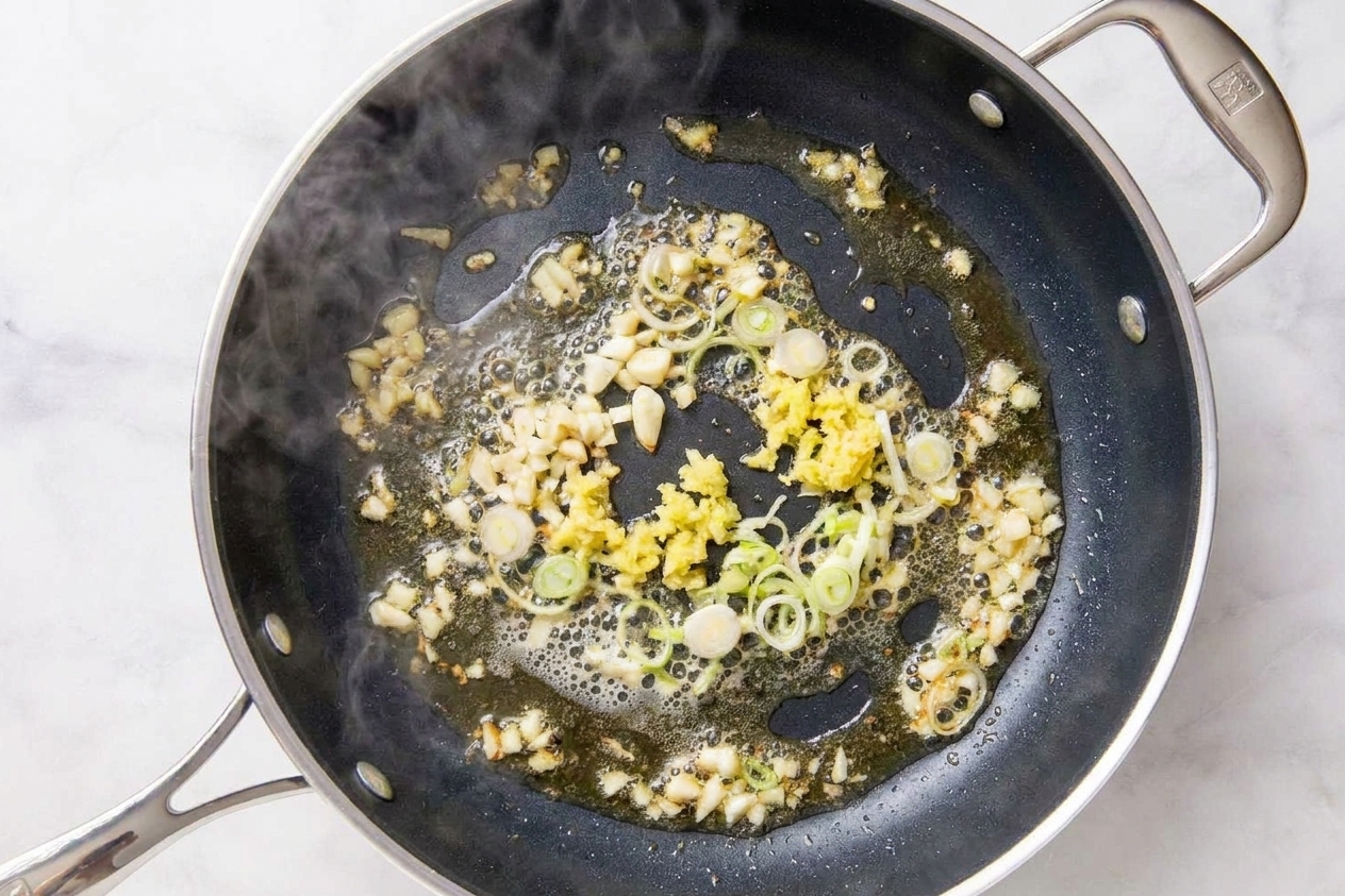 Garlic and ginger sizzling in a hot skillet with sliced scallion whites, just beginning to turn fragrant
